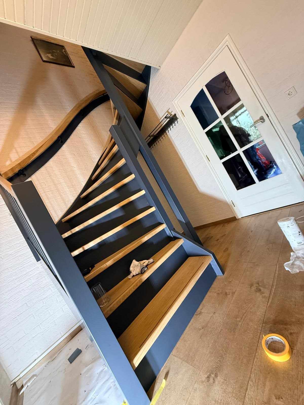 Blik naar beneden over de blauwe trap richting de hal met een deur met glasroeden