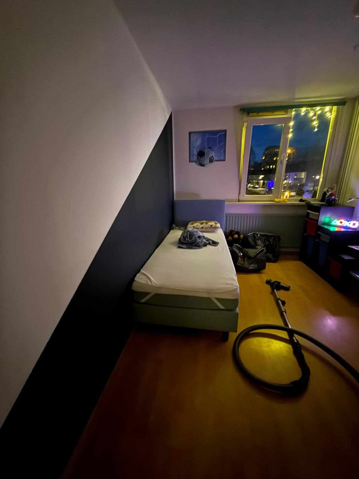 Kinderkamer met donkerblauwe schuine wand, bed en lichtjes langs het raam