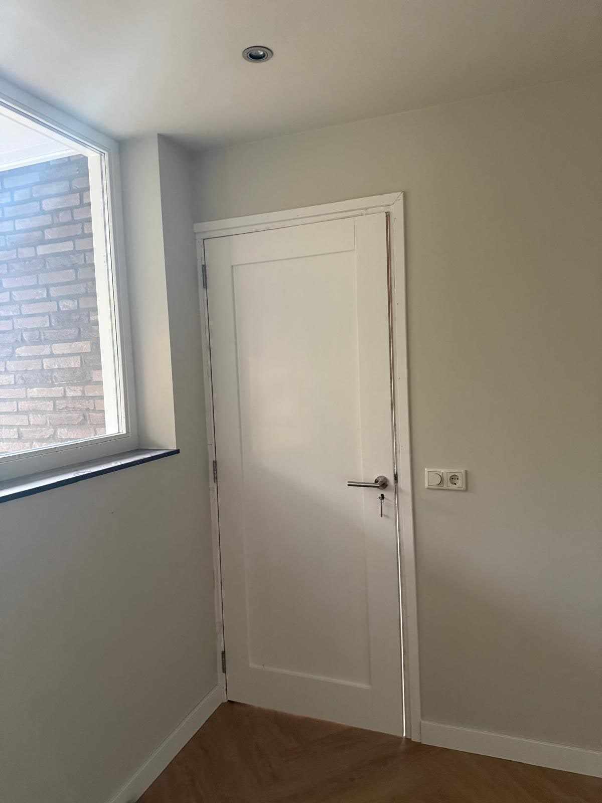 Witte binnendeur naast een raam in een kamer met beige wanden