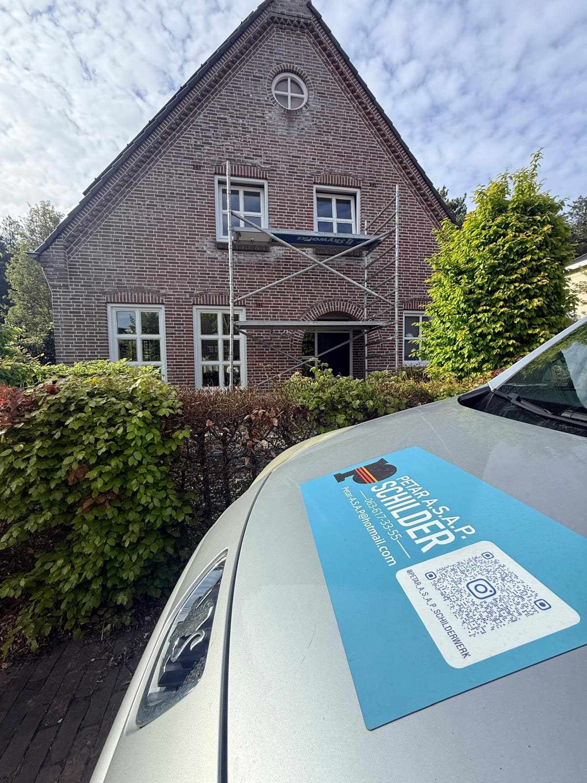 Magneetbord van Petar A.S.A.P. Schilderwerk op de motorkap, met achter de haag de bakstenen woning en de steiger