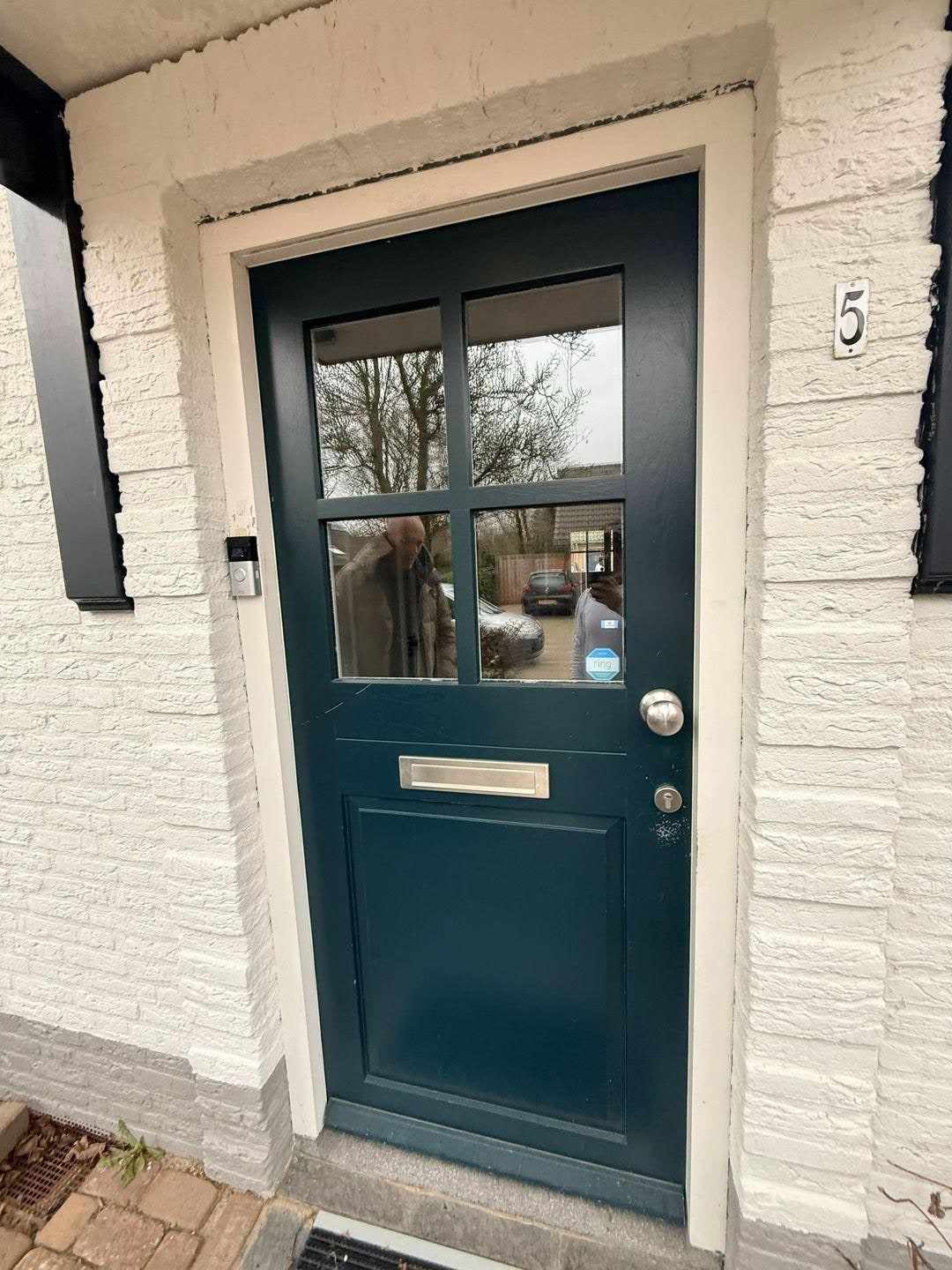 Donkergroene voordeur met glasroeden en brievenbus in de witte bakstenen gevel