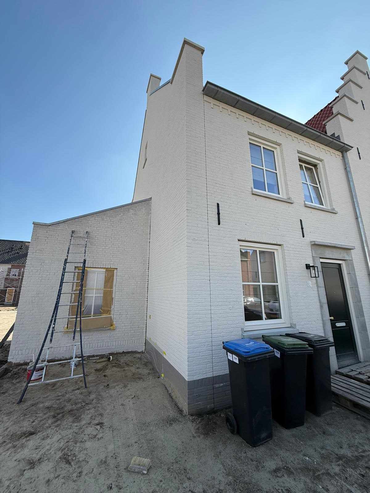 Wit geschilderde nieuwbouwwoning met ladder tegen de gevel en een nog onafgewerkte tuin