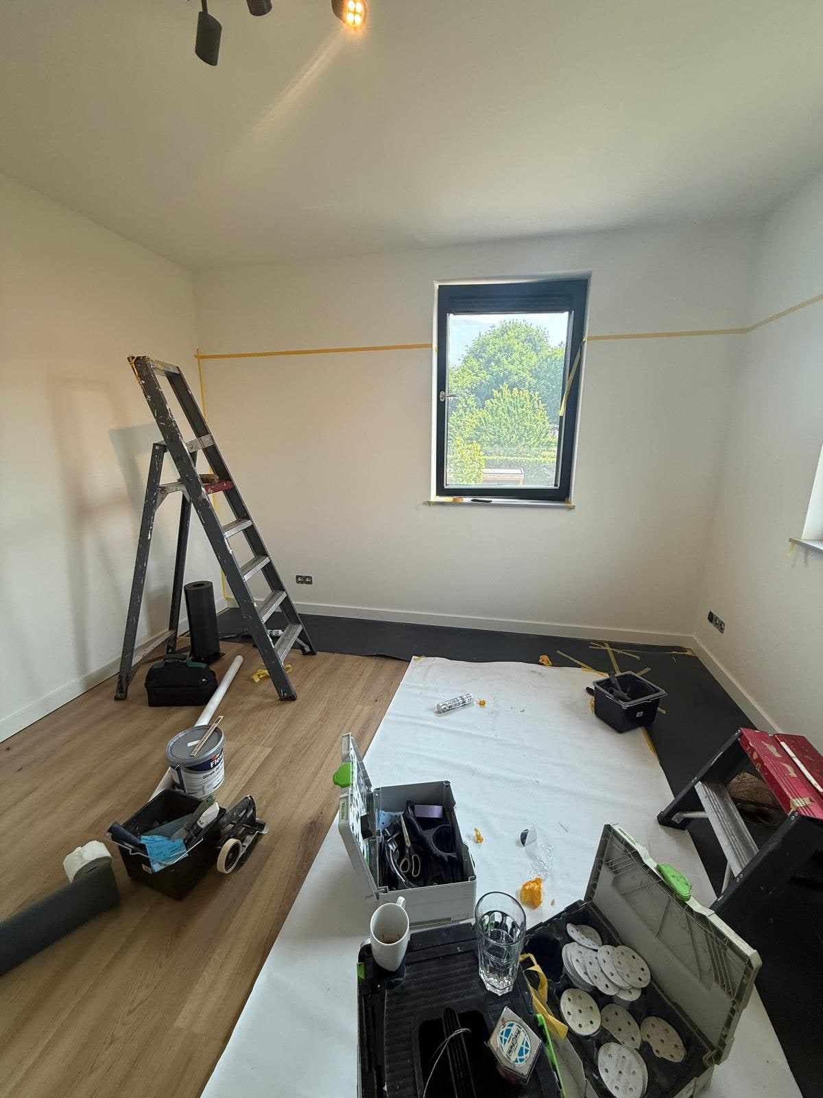 Lege kamer met witte wanden, een trapladder en gereedschap op de afgedekte vloer