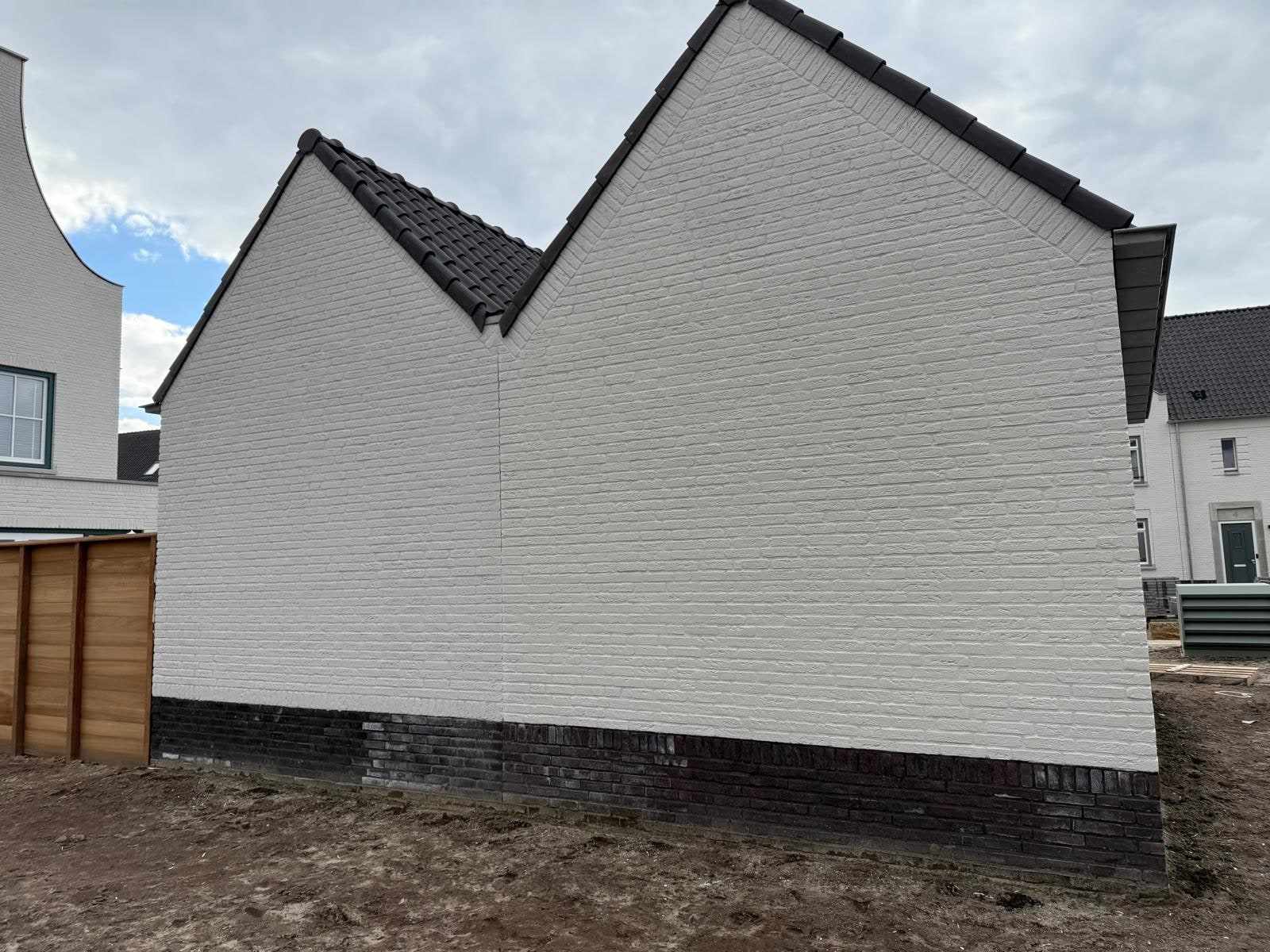 Wit geschilderde garagegevel met twee puntdaken, naast een houten schutting