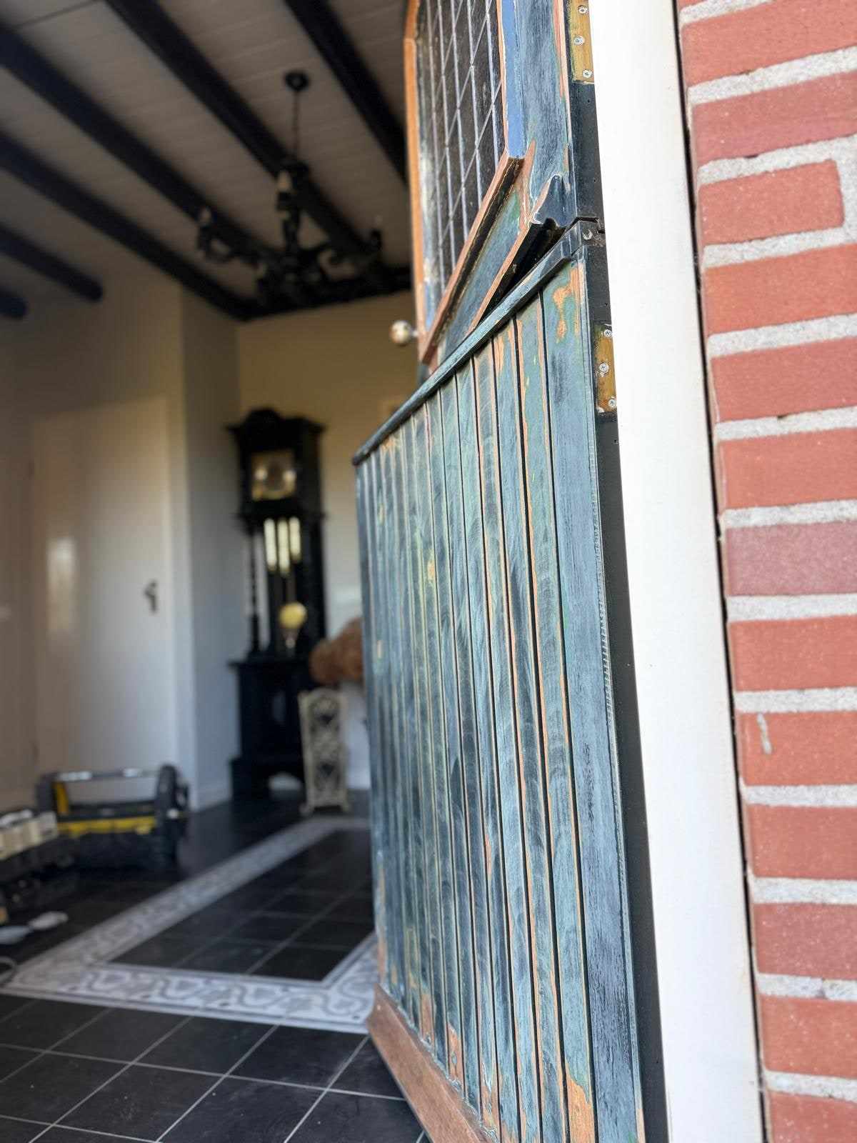 Openstaande oude deur met kale plekken in de verf, de hal met tegelvloer erachter