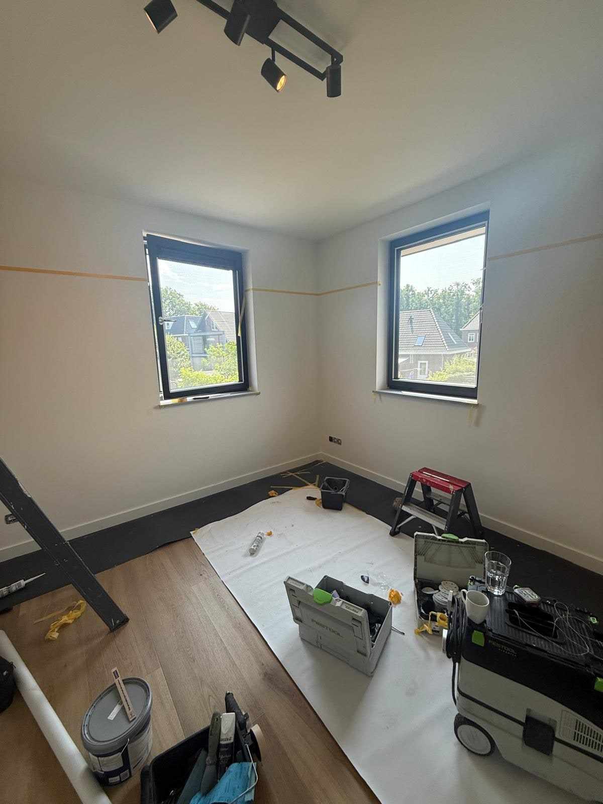 Kamer met twee ramen, afdekfolie op de vloer en verfgereedschap klaargezet