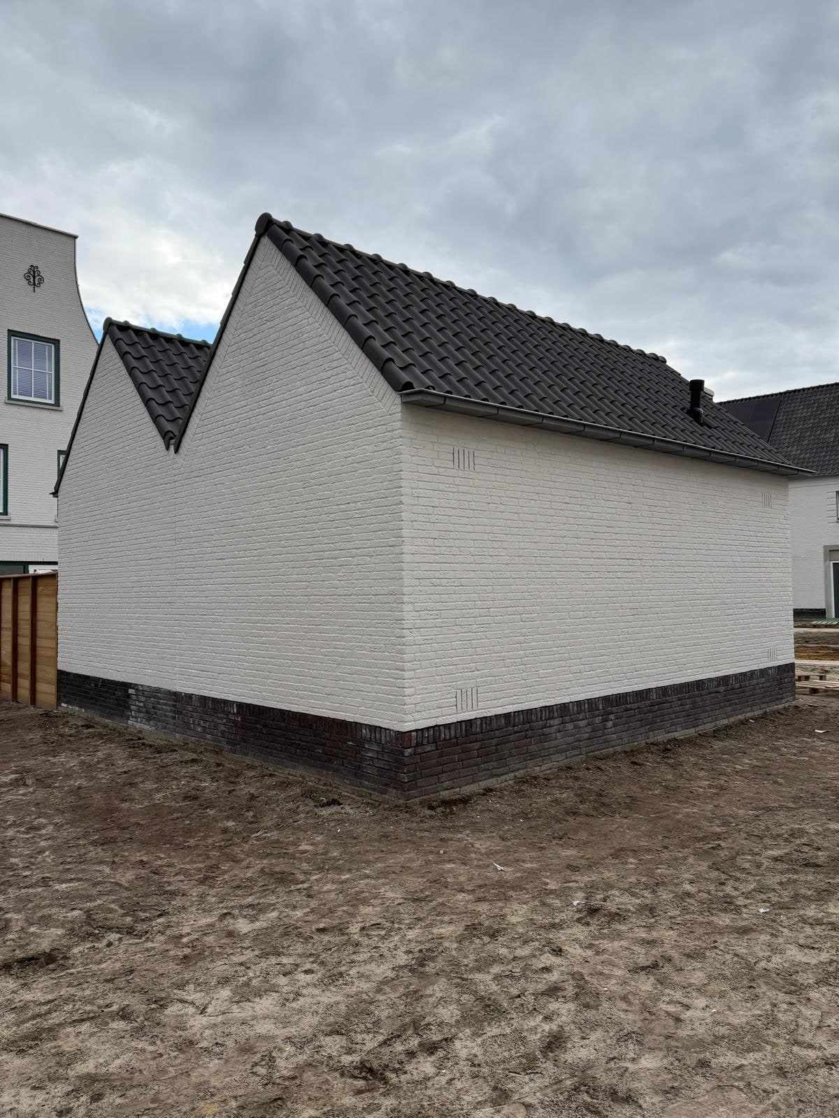 Zijkant van de witte garages met donkere plint boven het nog kale zand