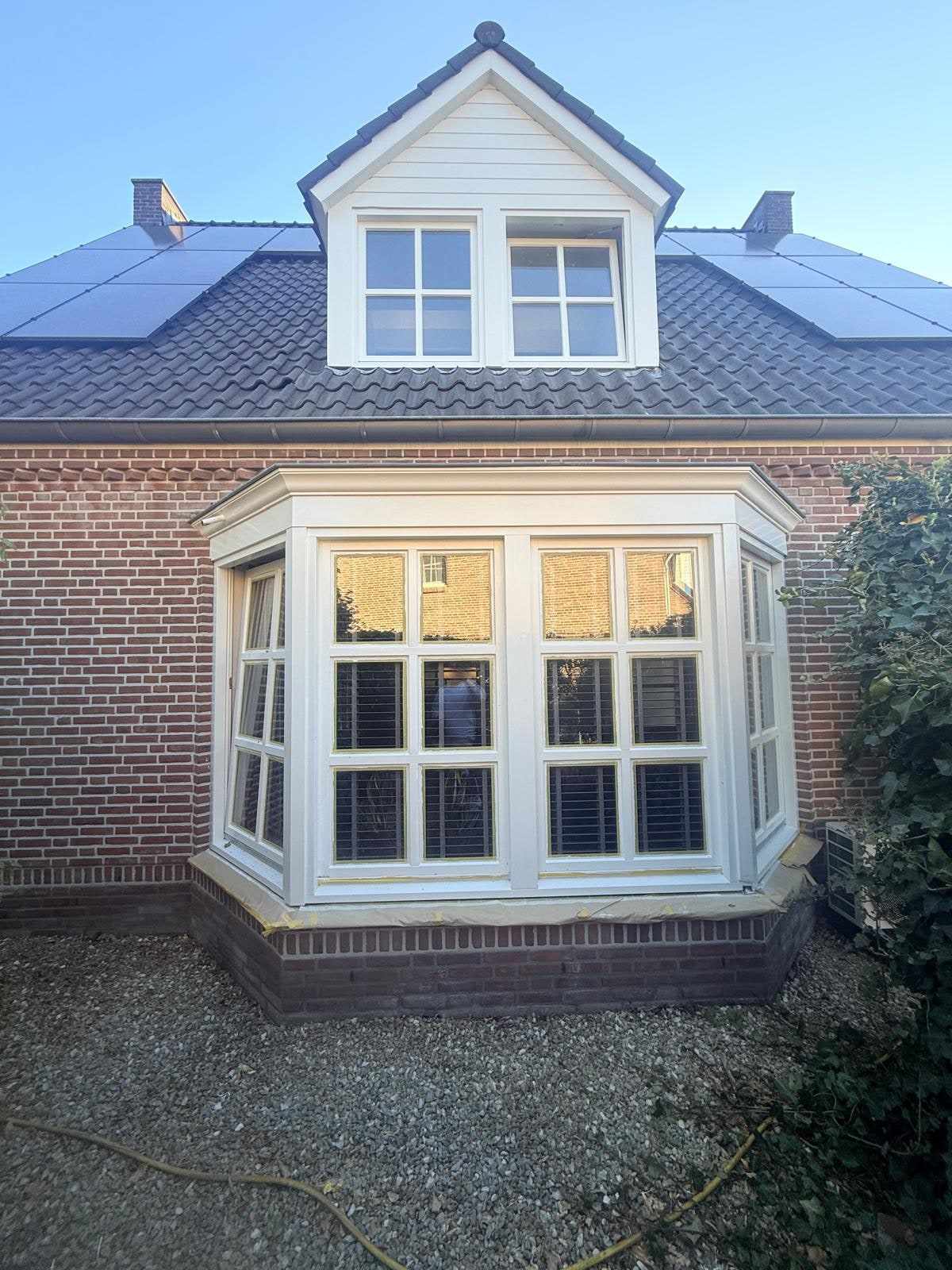 Erker en dakkapel met verse witte kozijnen in de zon, gezien vanaf de tuin