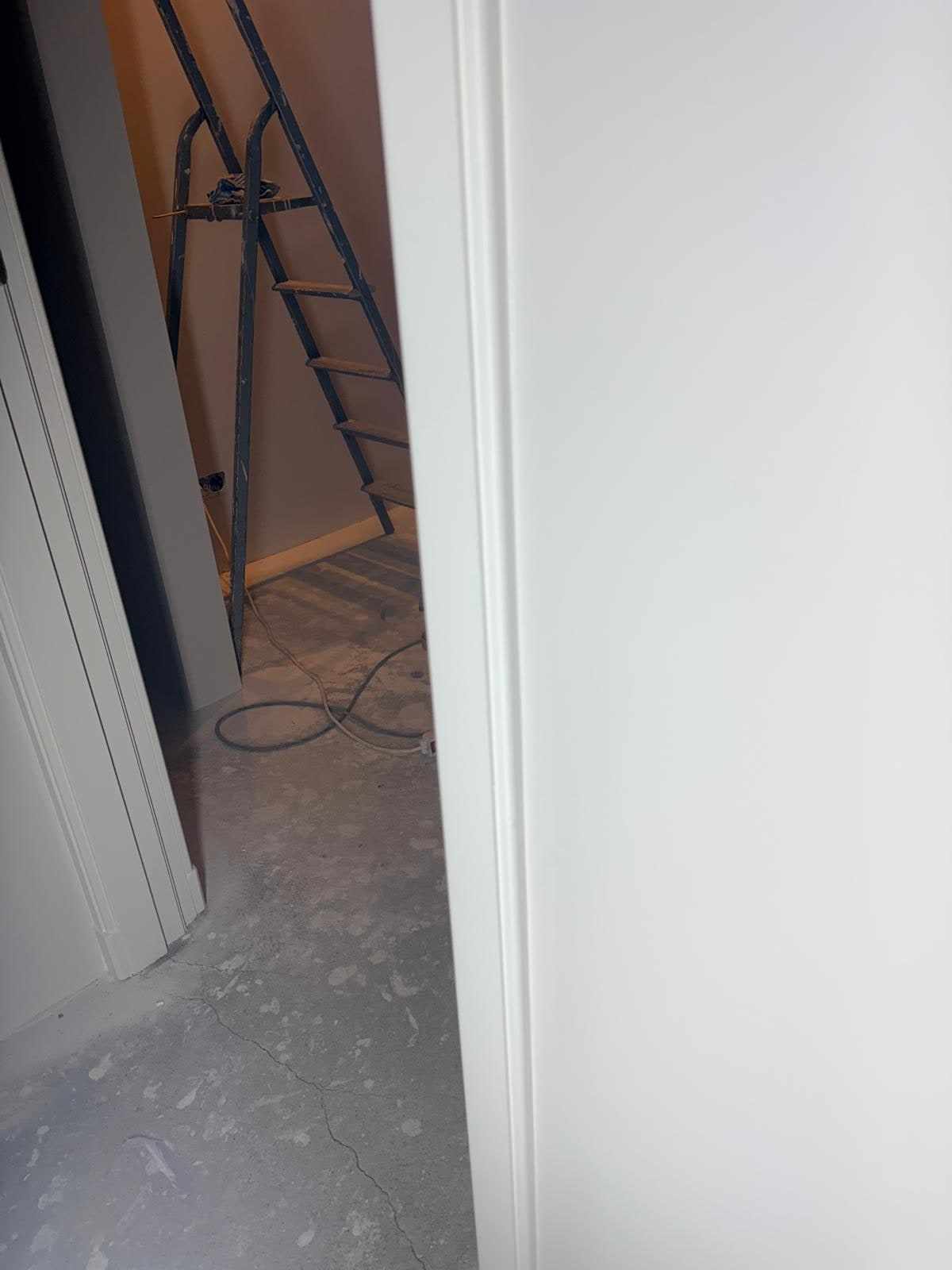 Witte deur in de hal met een ladder en verlengsnoer op de dekvloer erachter