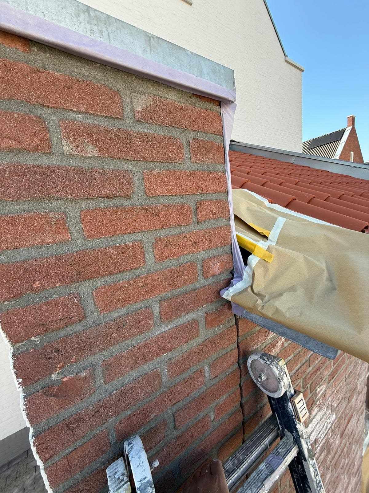 Detail van de aansluiting tussen metselwerk en dakrand, afgeplakt met papier