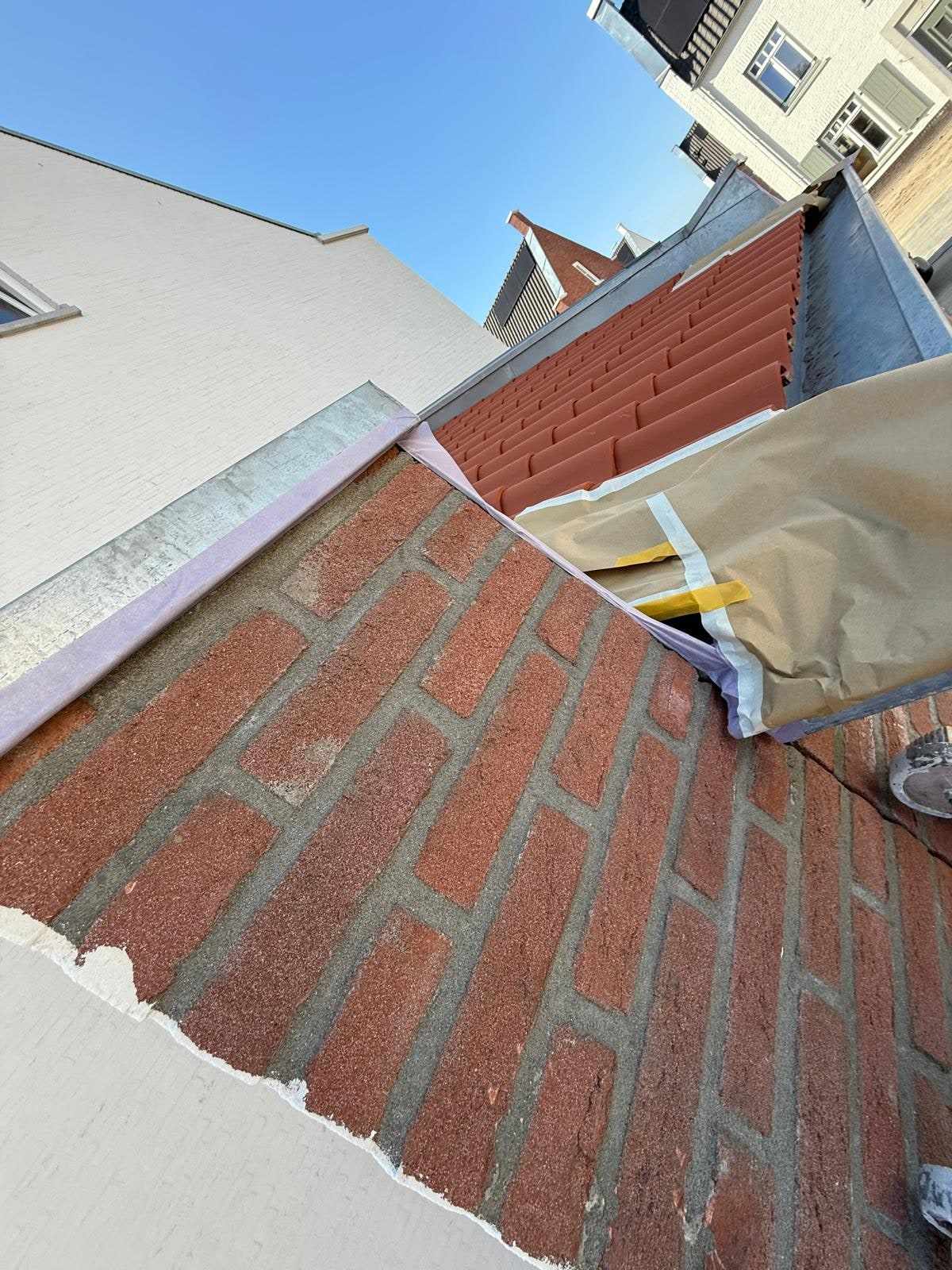 Afgeplakte dakpannen langs de gevel waar de witte verf tot aan de rand doorloopt