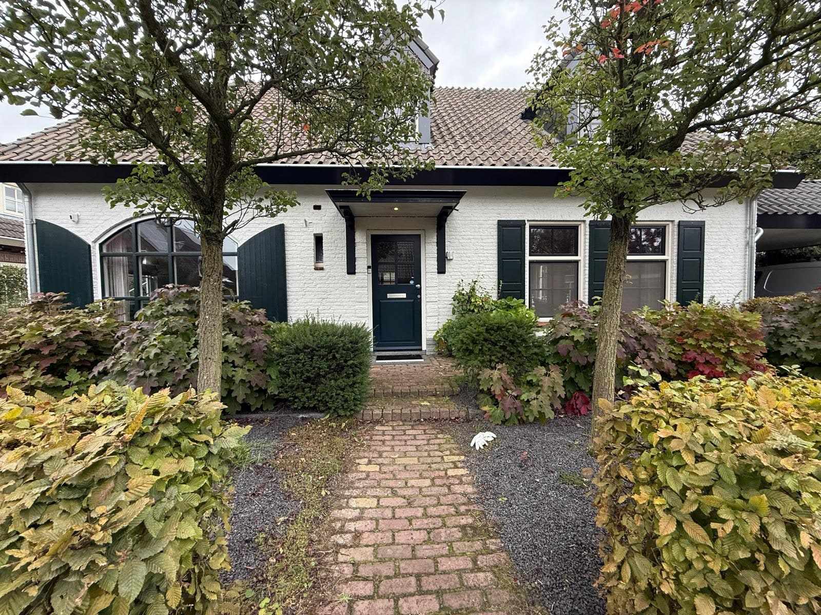 Wit geschilderde woning met donkergroene luiken en een groene voordeur aan de straatzijde