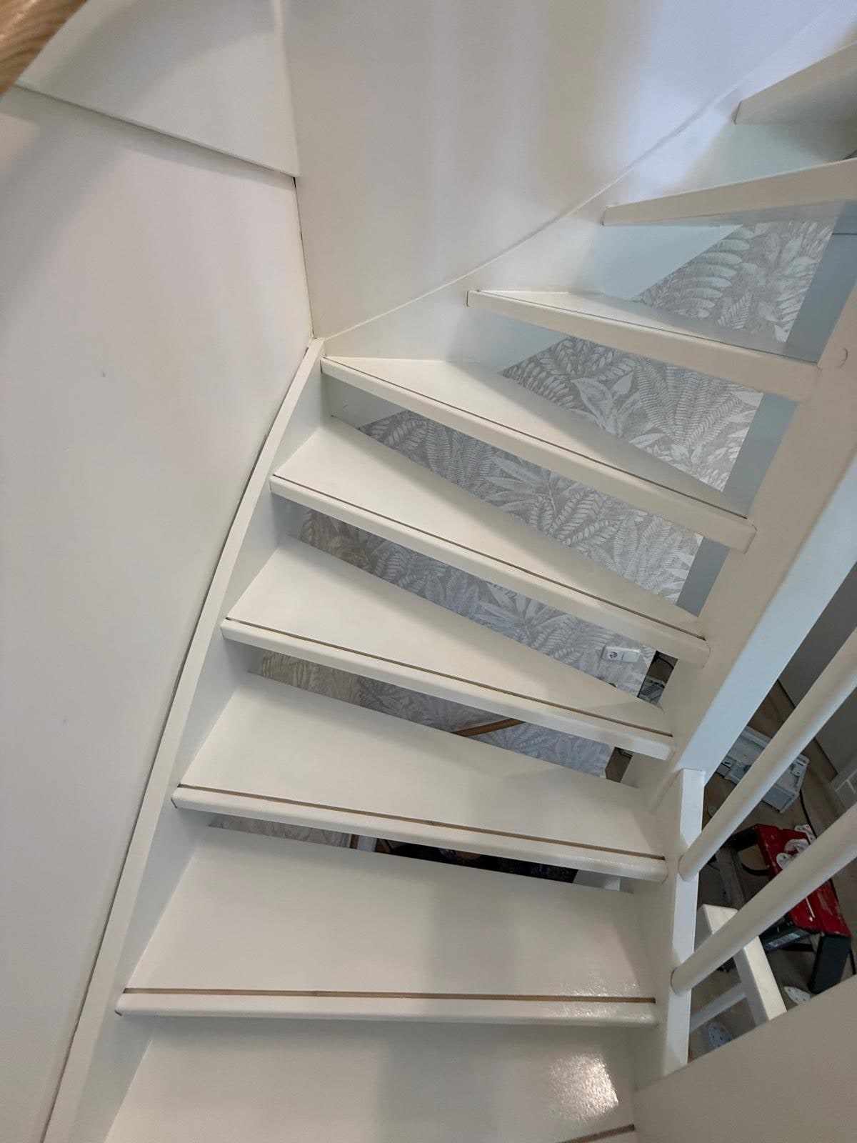 Wit gelakte kwartslagtrap met witte balustrade tegen een lichte behangen wand