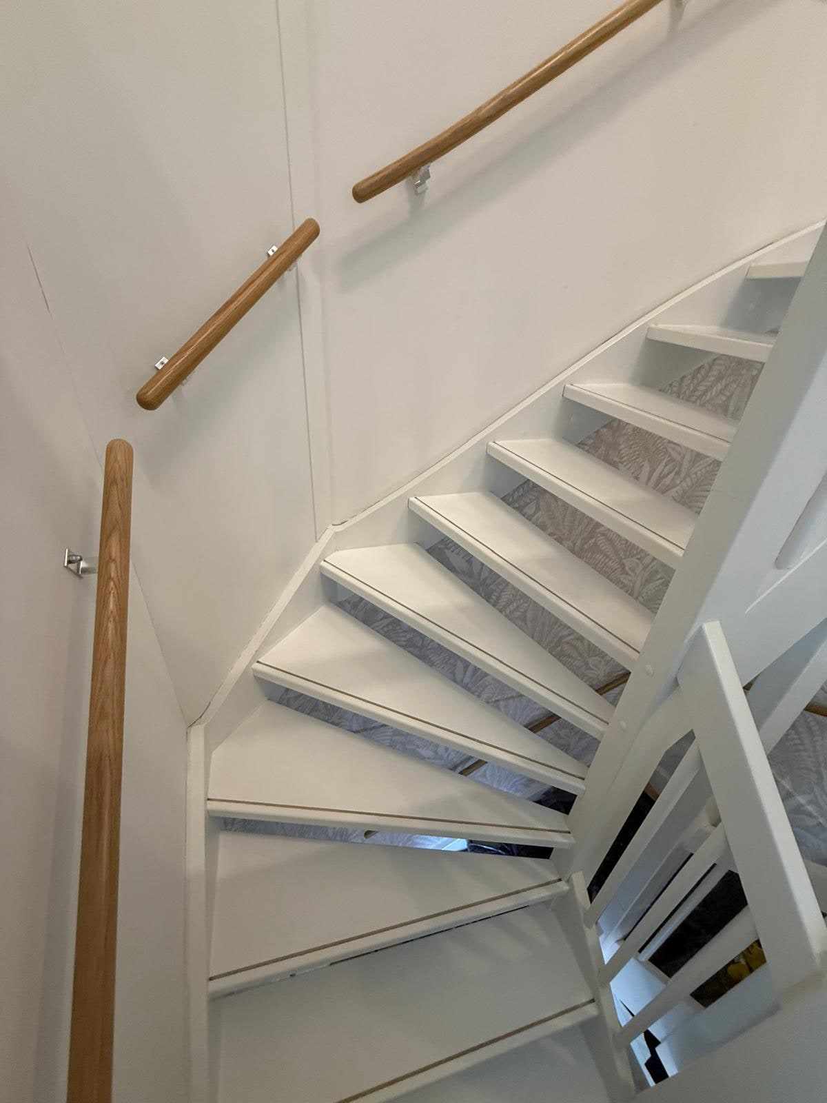 Blanke houten handlijst aan de wand naast de wit geschilderde trap en balustrade