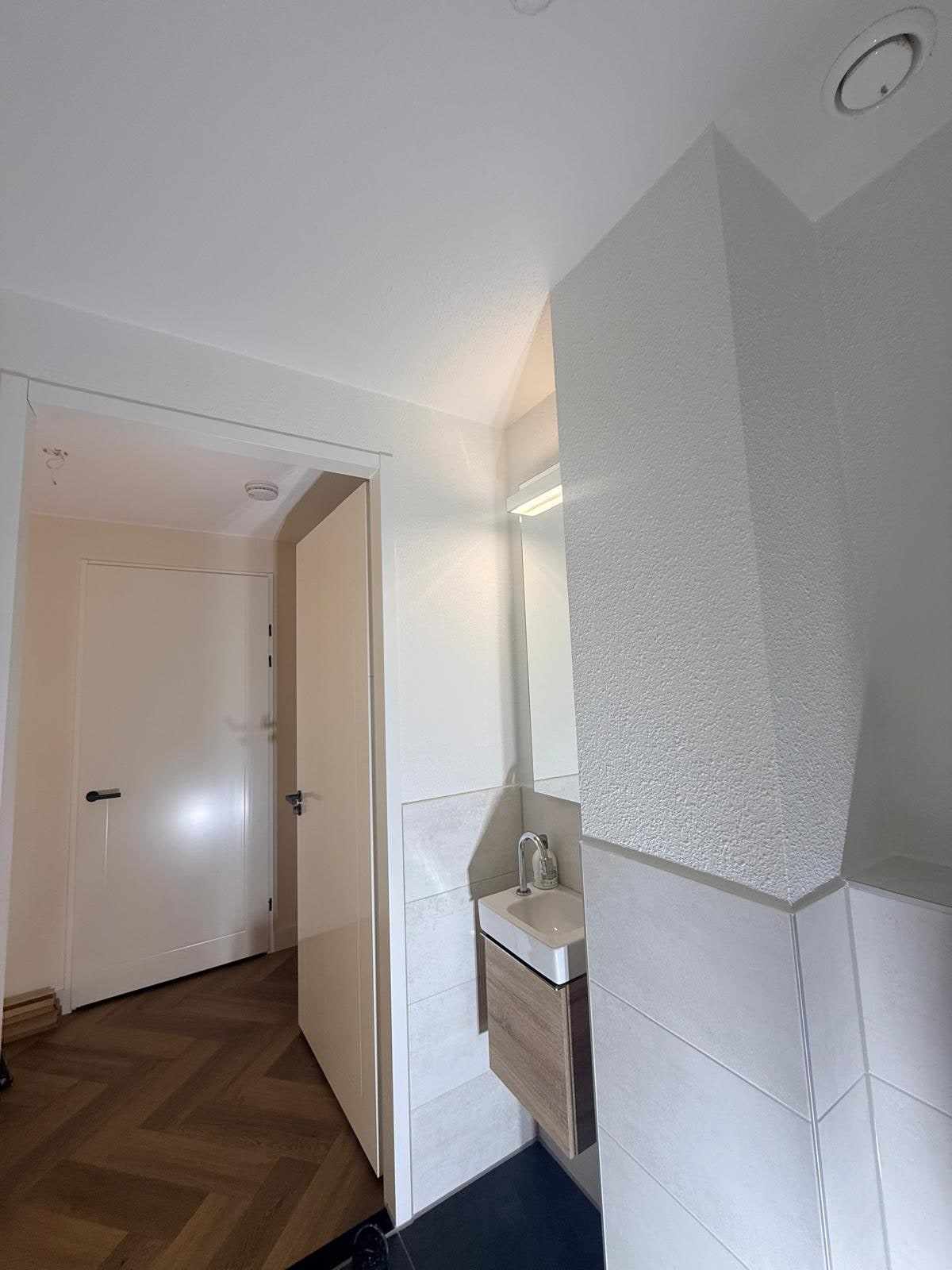 Witte wanden en plafond in de toiletruimte, met doorkijk naar de visgraatvloer
