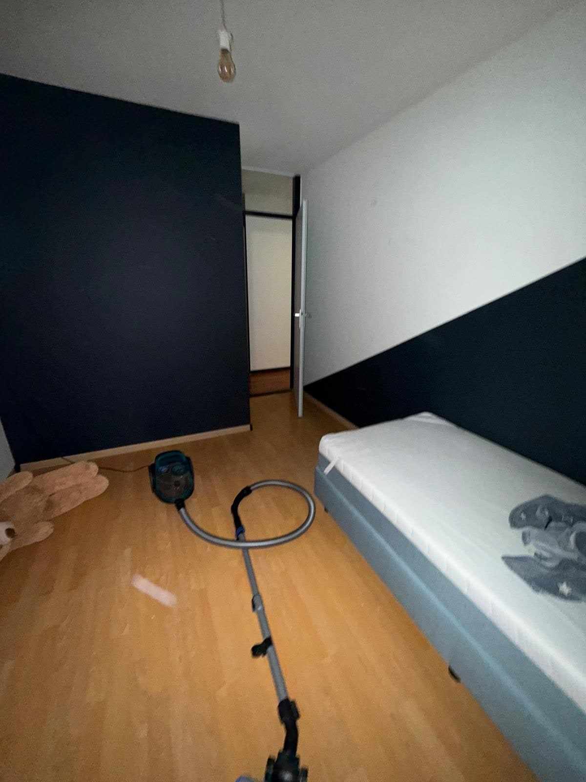 Donkerblauw geschilderde wand met kastdeur, naast het bed in de kinderkamer