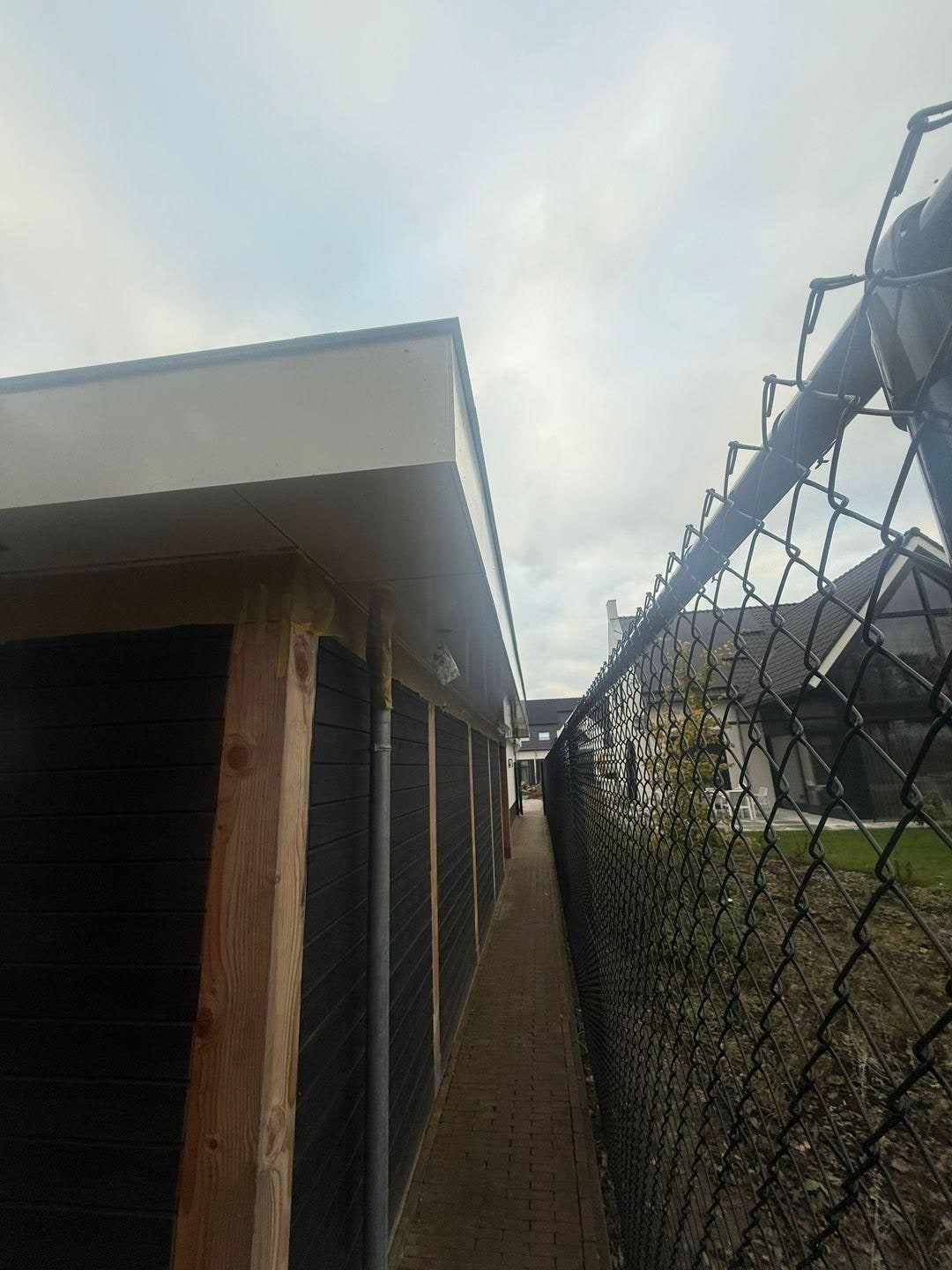 Zijkant van de overkapping met witte dakrand en houten staanders langs het hekwerk