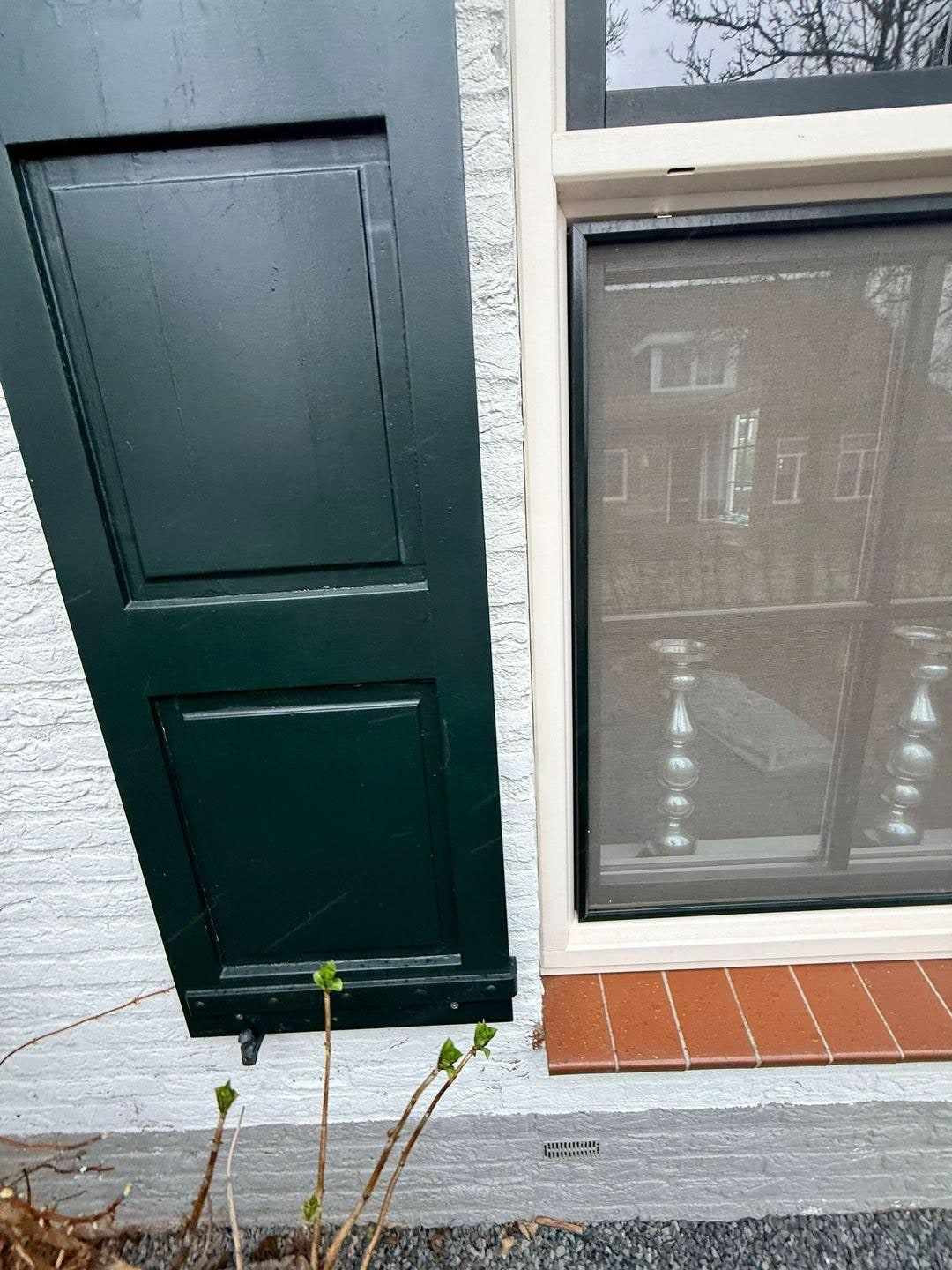 Openstaand donker luik naast een raam met witte roeden in de witte gevel