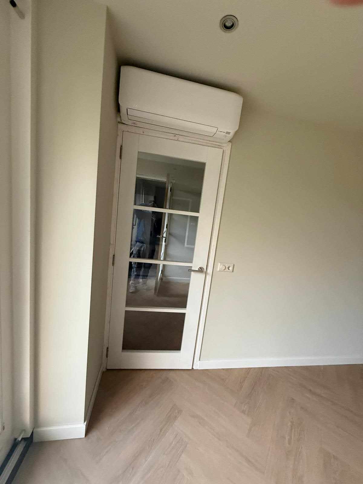 Witte deur met glasroeden onder een airco-unit in een lichte kamerhoek