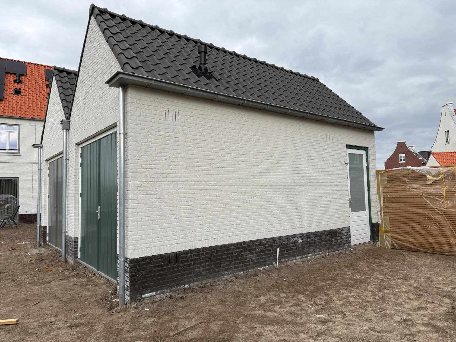 Witte garage met donkergroene deur, gezien vanaf de zijkant van het bouwterrein