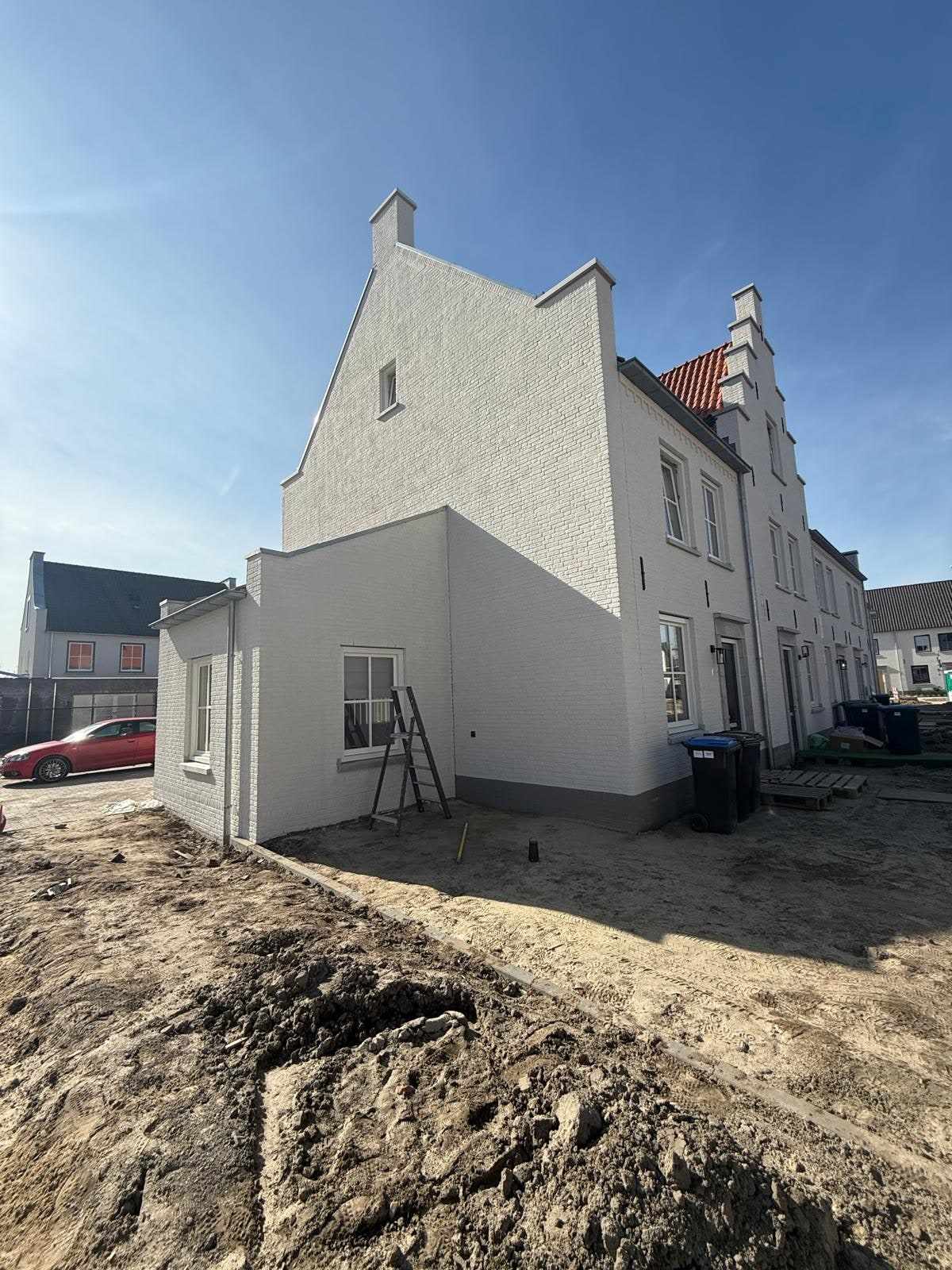 Witte zijgevel met trapgevel en aanbouw, gezien vanaf het zandpad