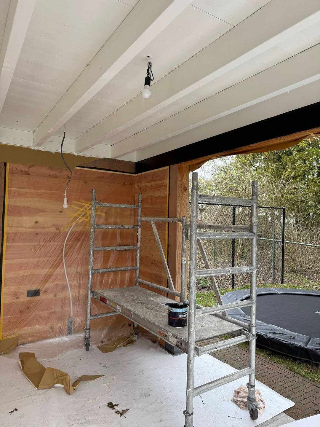 Wit geschilderde plafondschroten onder de overkapping, met rolsteiger en afdekzeil
