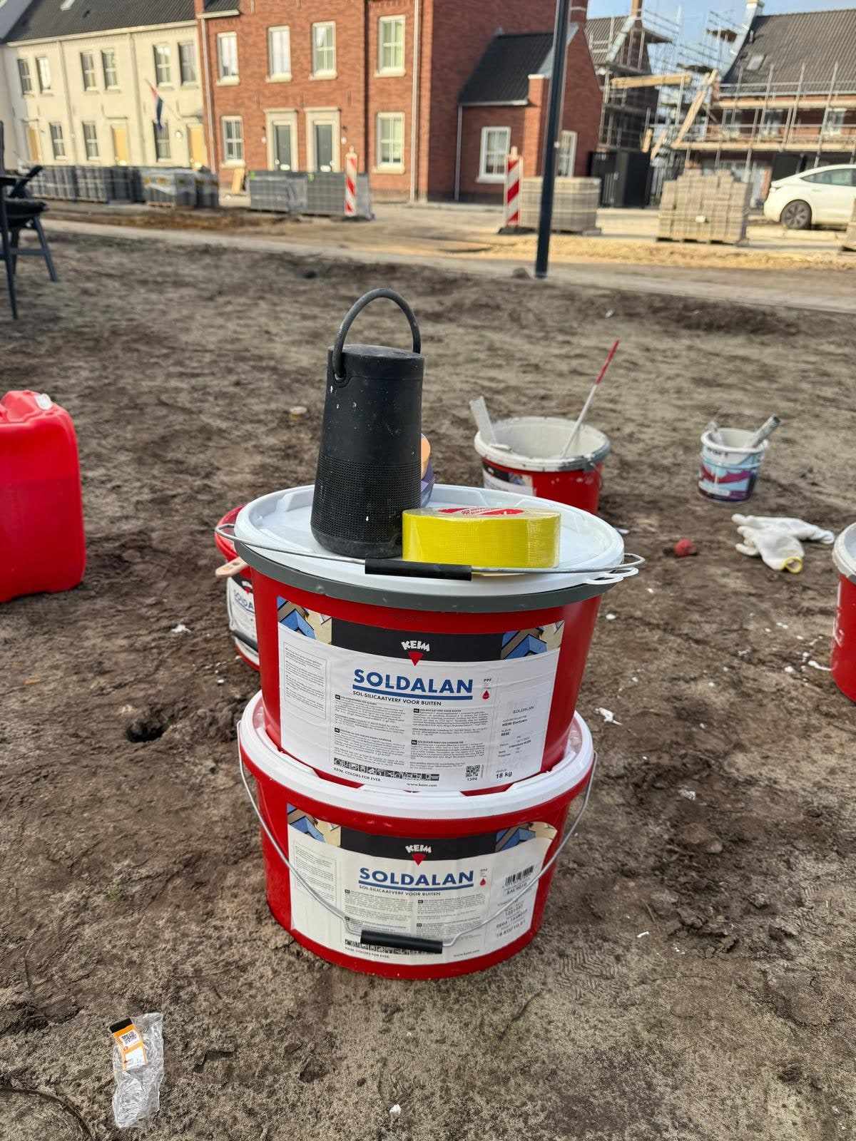 Verfemmers en gereedschap op het zand voor de garages tijdens het schilderwerk