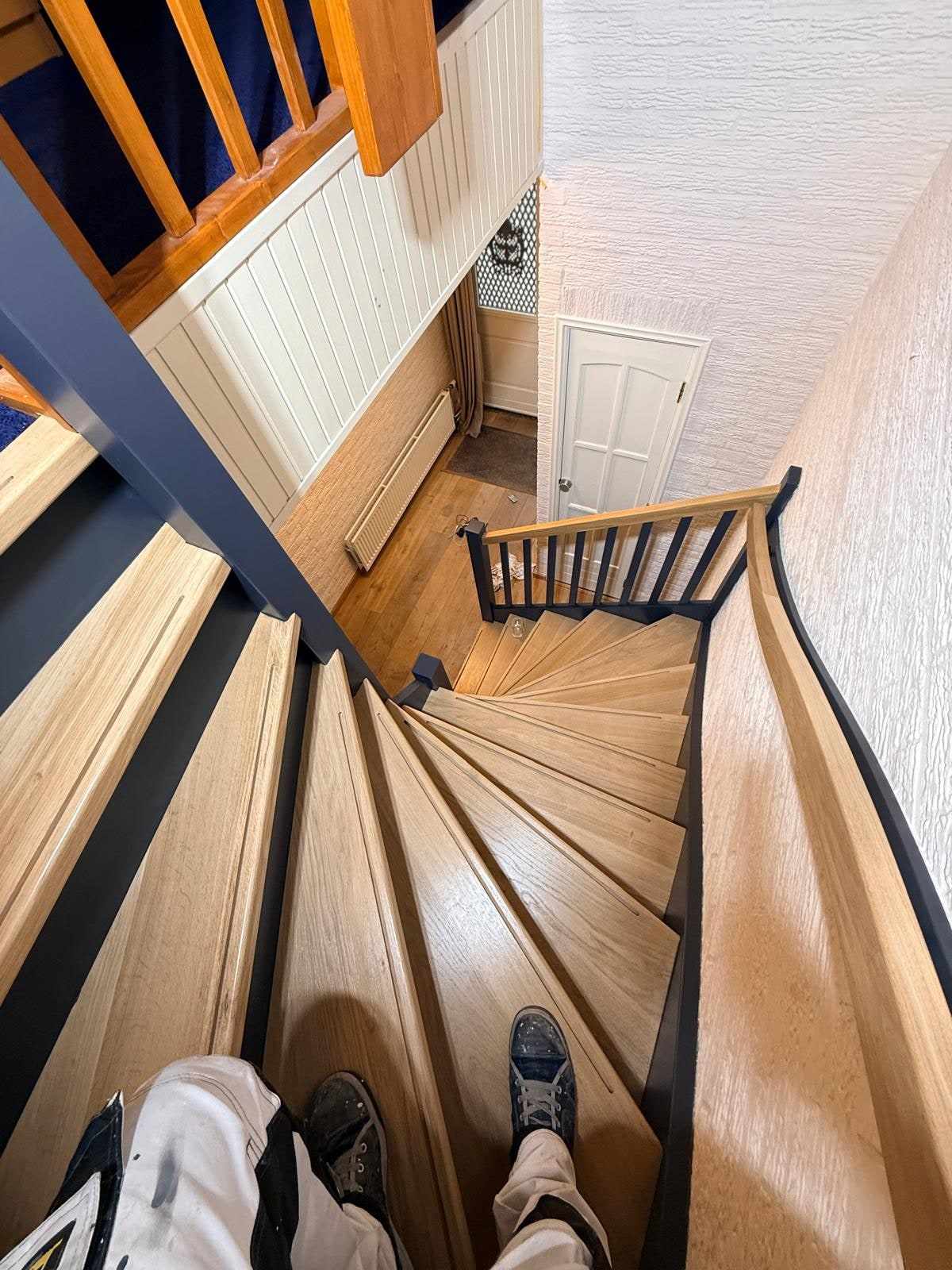 Draaitrap van bovenaf met eiken treden en donkerblauwe balustrade langs de wand