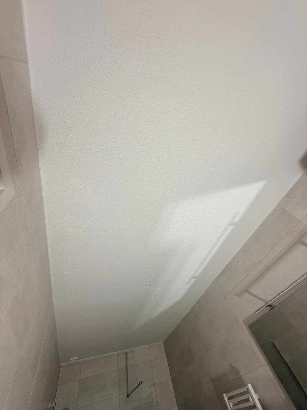 Wit geschilderd plafond boven de douche, strak afgezet tegen de tegelwand