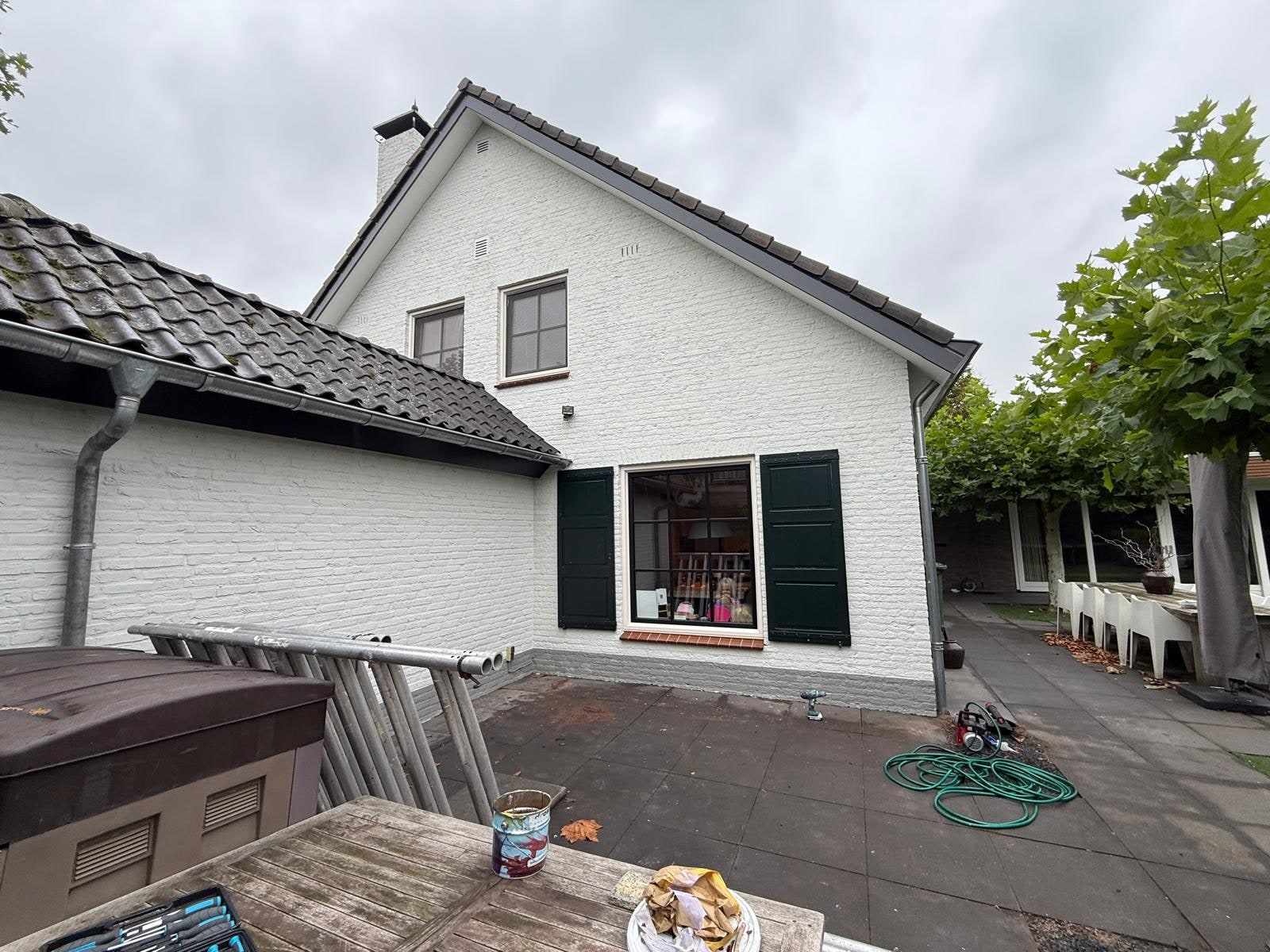 Achtergevel wit geschilderd met donkergroene luiken langs het keukenraam
