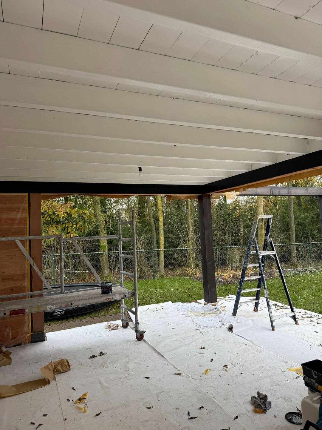 Witte plafondschroten met donkere balken, ladder en afdekzeil op het terras