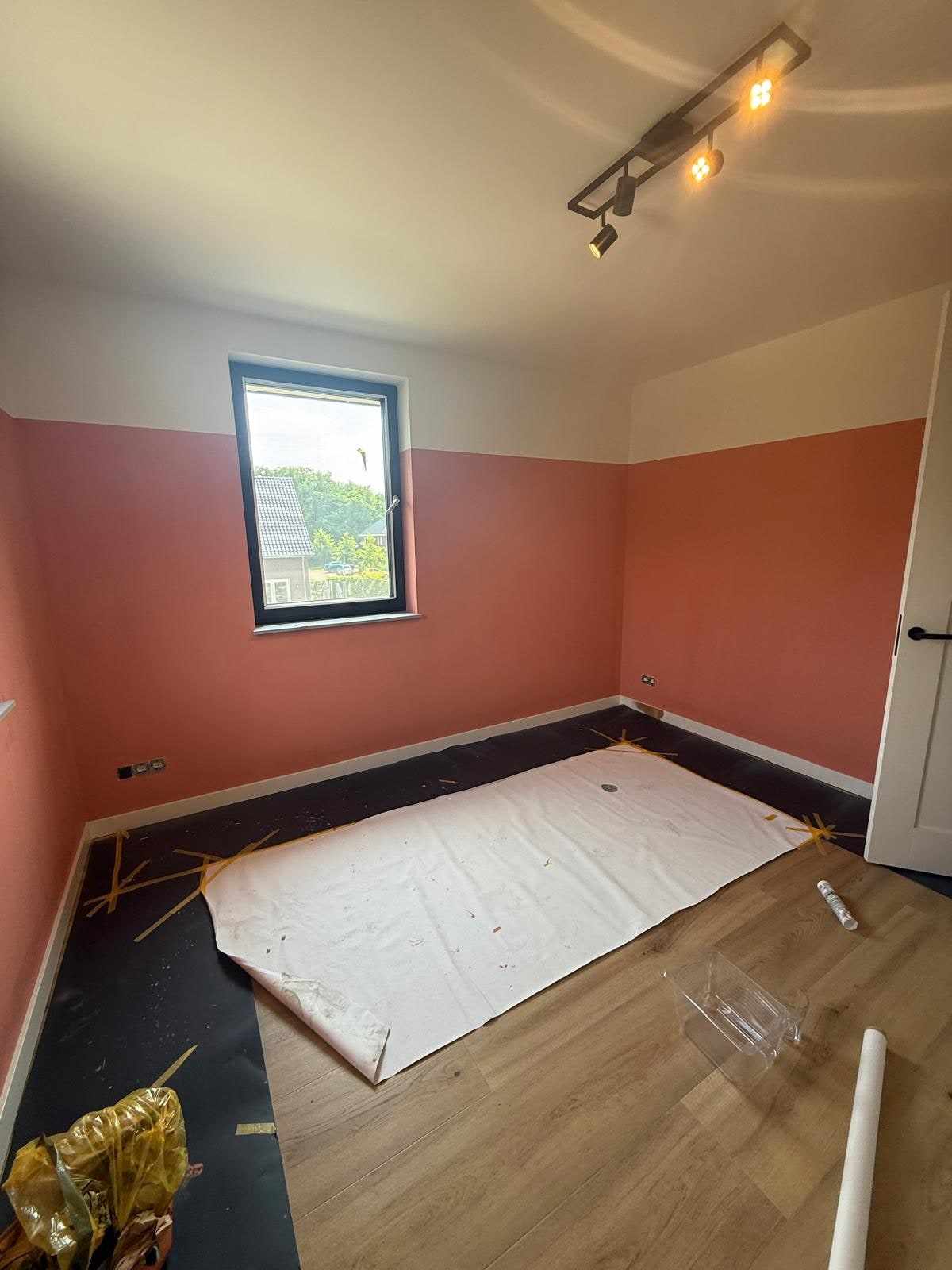 Kamerhoek met terracotta wand tot ooghoogte en een wit plafond met spotrail