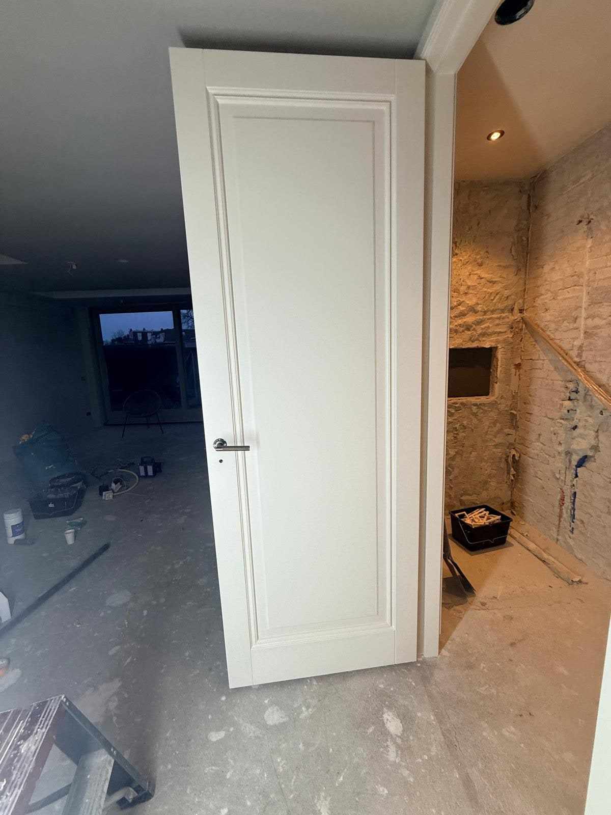 Wit gelakte paneeldeur voor een kamer met een onafgewerkte bakstenen wand