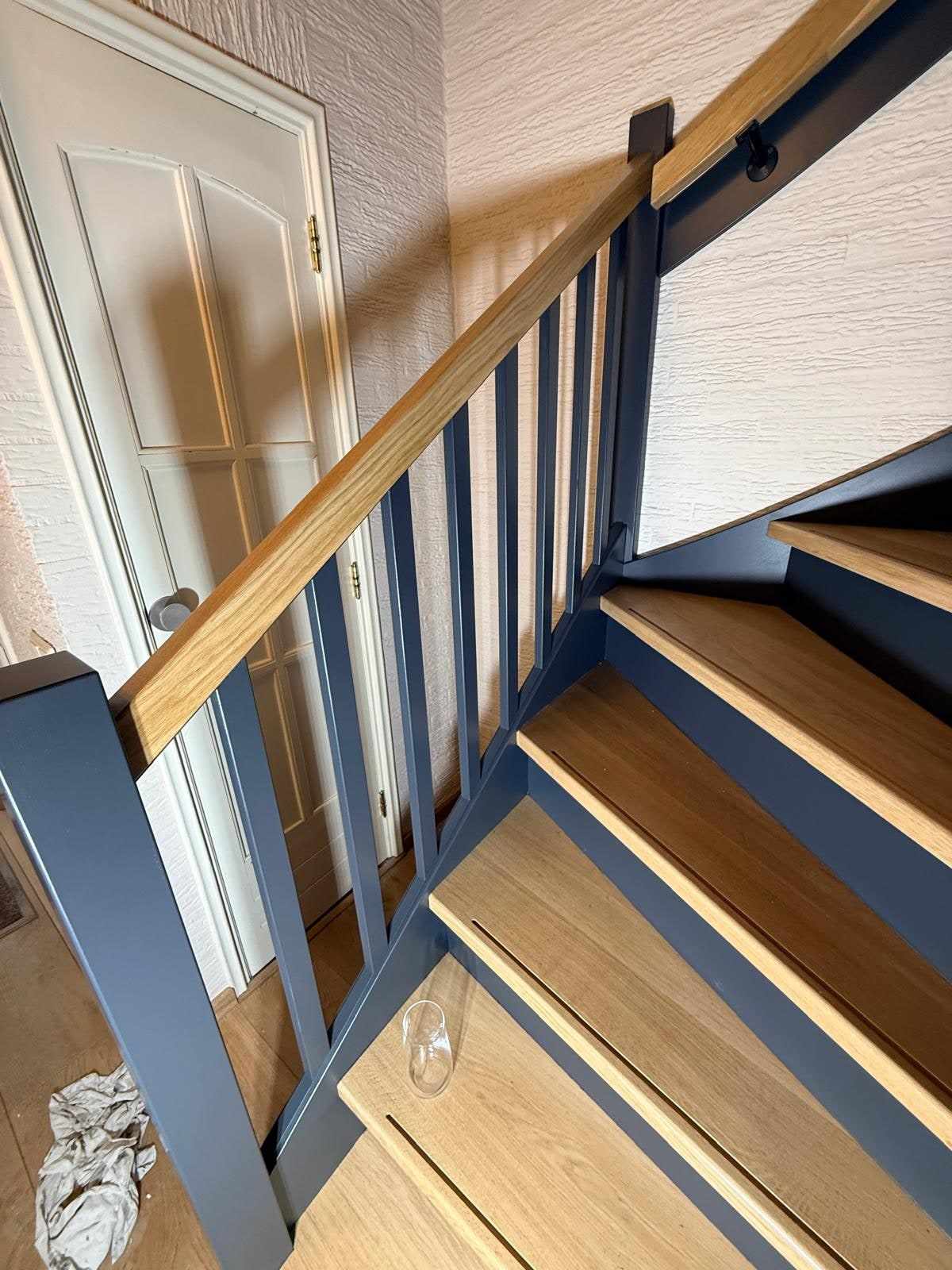 Onderaanzicht van de trap met blauwe balustrade naast een witte paneeldeur