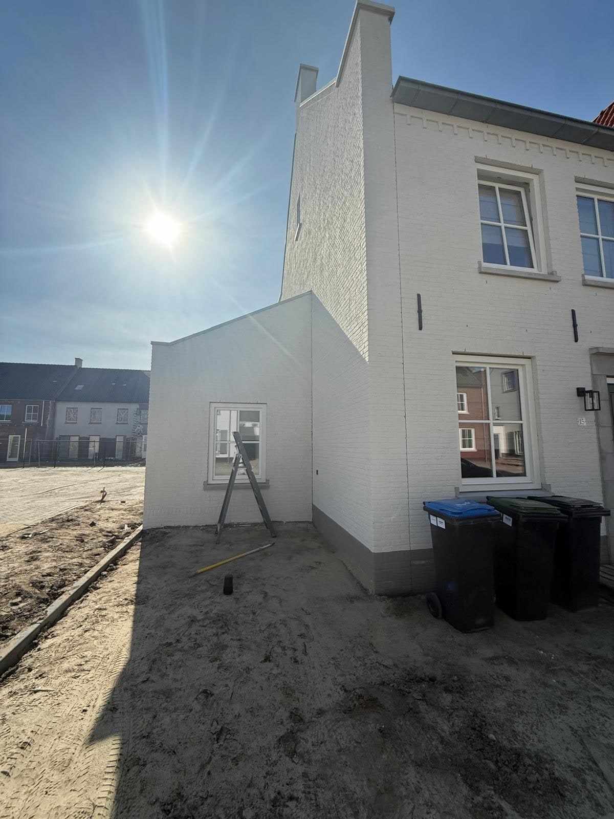 Witte gevel van de nieuwbouwwoning in tegenlicht, met de zon boven het dak