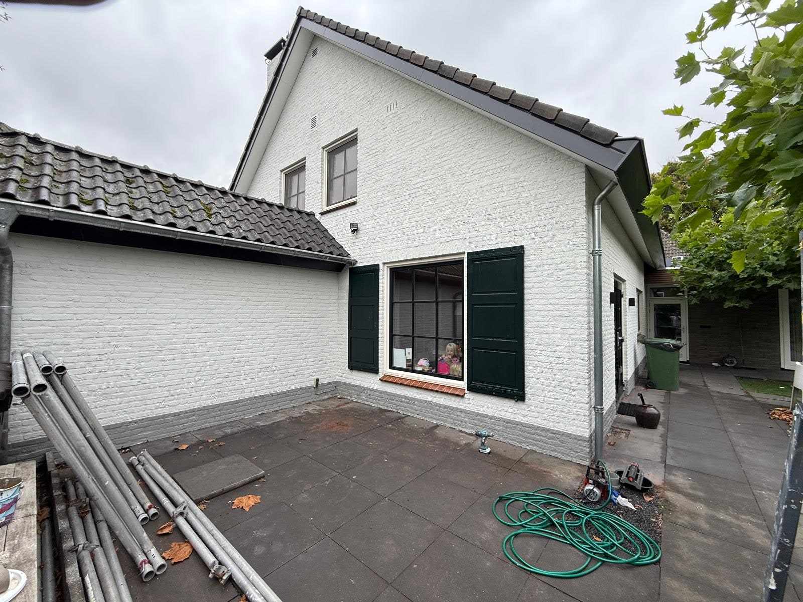 Wit geschilderde achtergevel met donkergroene luiken, steigerdelen nog op het terras