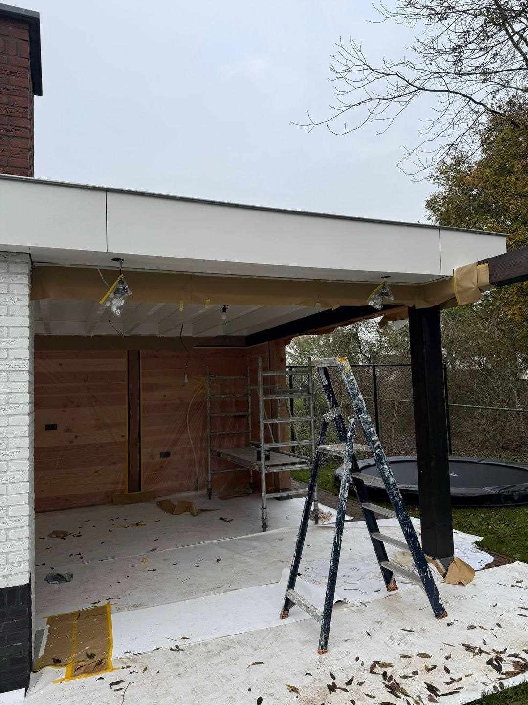Overkapping tegen de witte gevel met rolsteiger en afgedekte vloer eronder