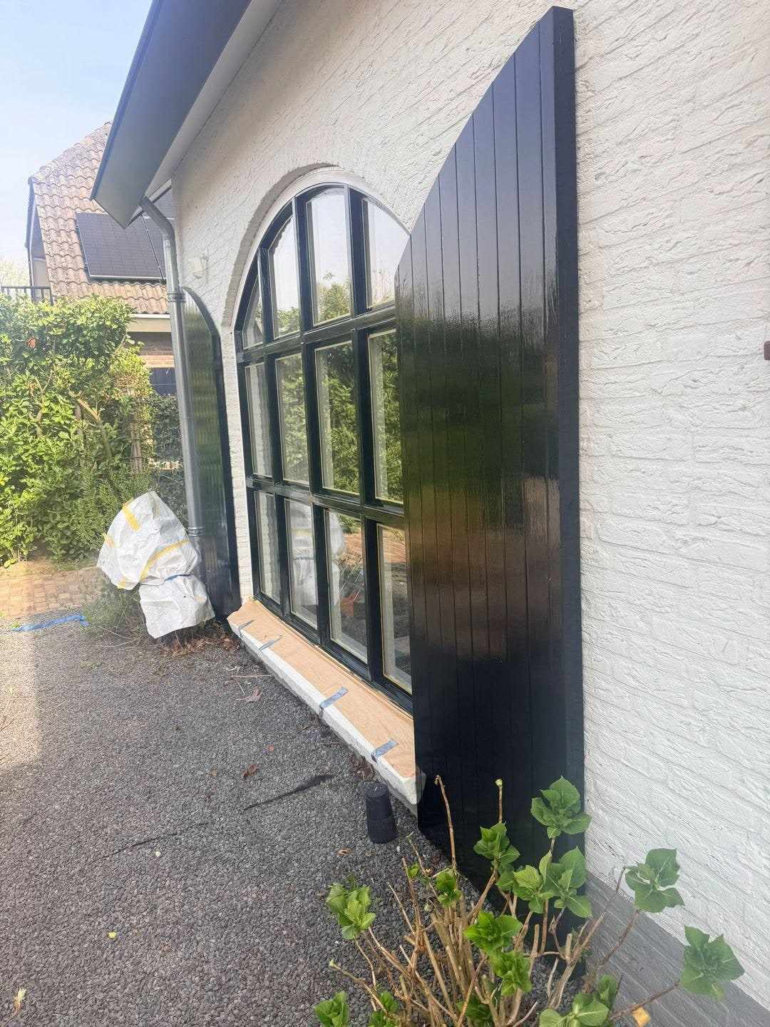 Boogvenster met zwarte roeden naast een donker geschilderd houten paneel