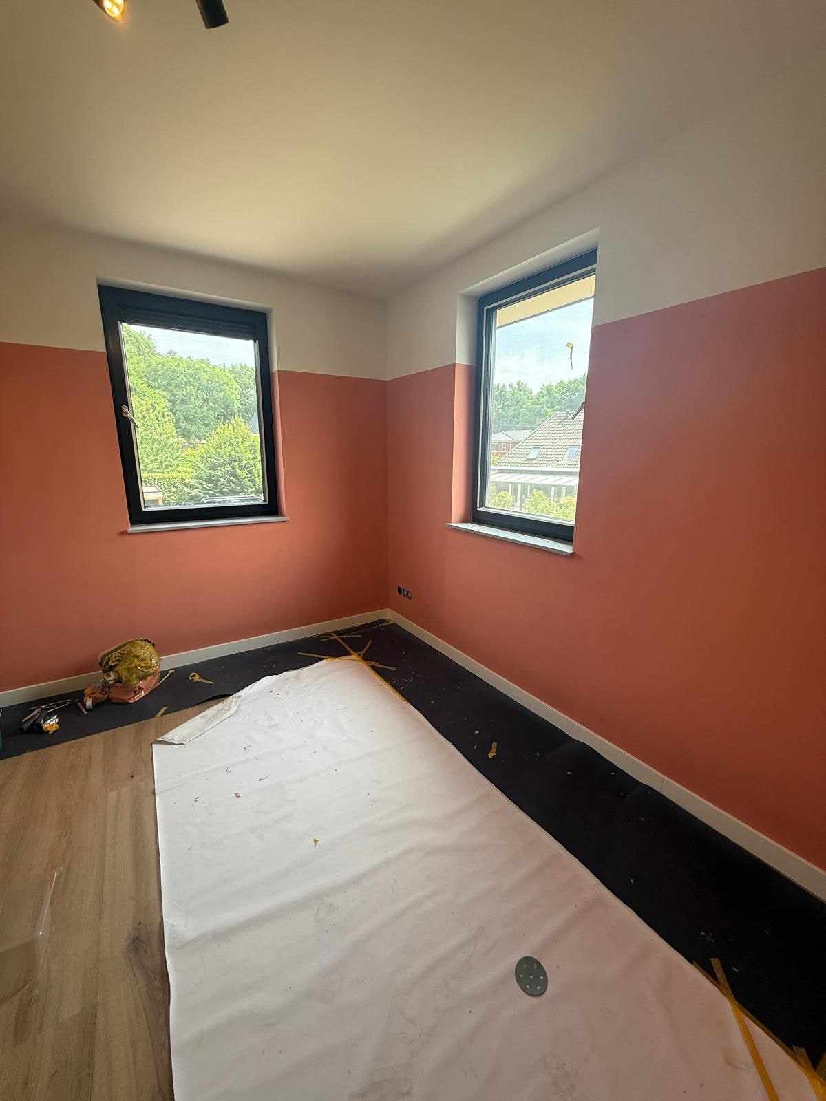 Kamer met terracotta onderwand, witte bovenwand en zwarte kozijnen bij twee ramen