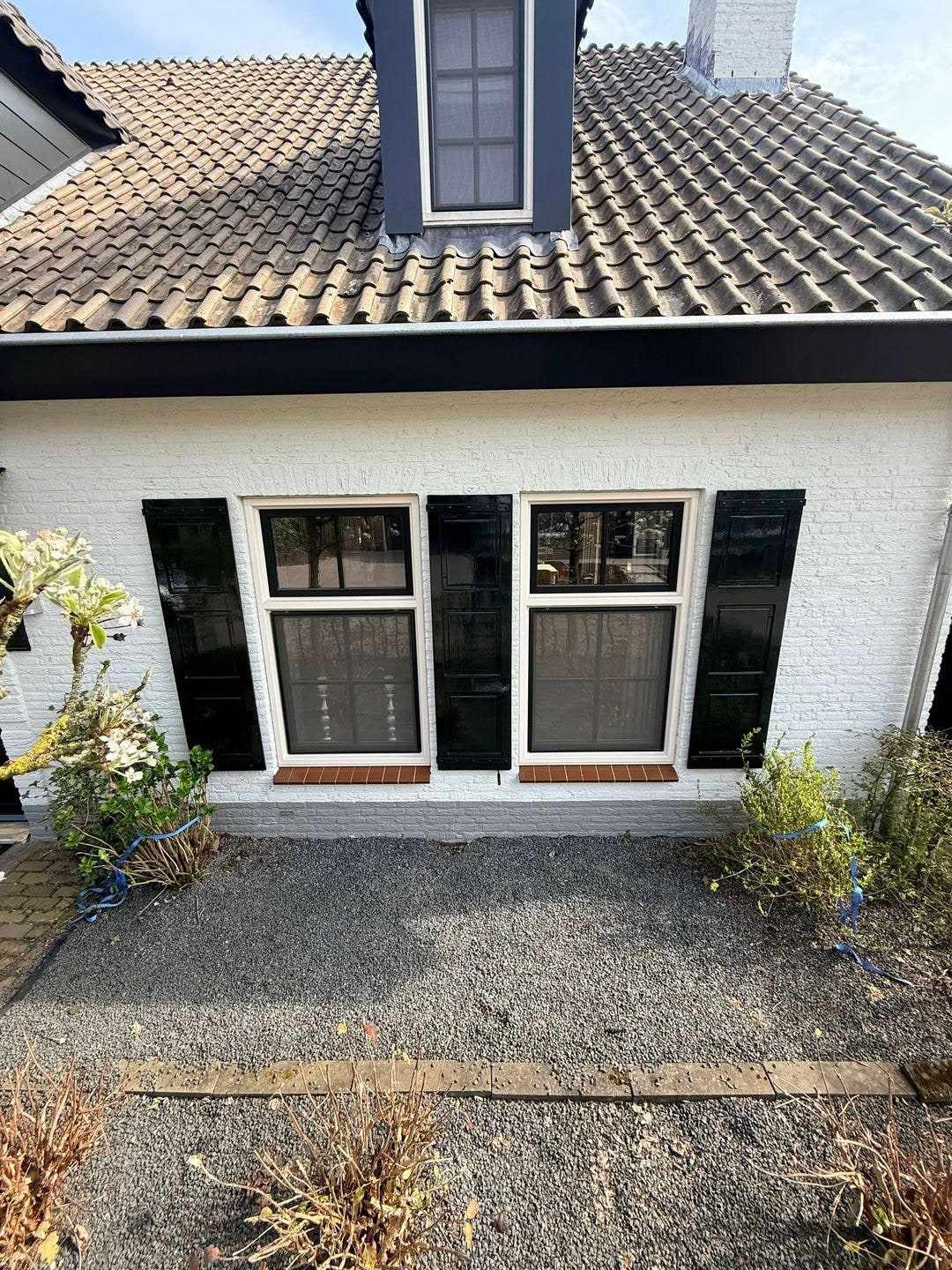 Twee ramen met donkere luiken en witte kozijnen boven een rode raamdorpel