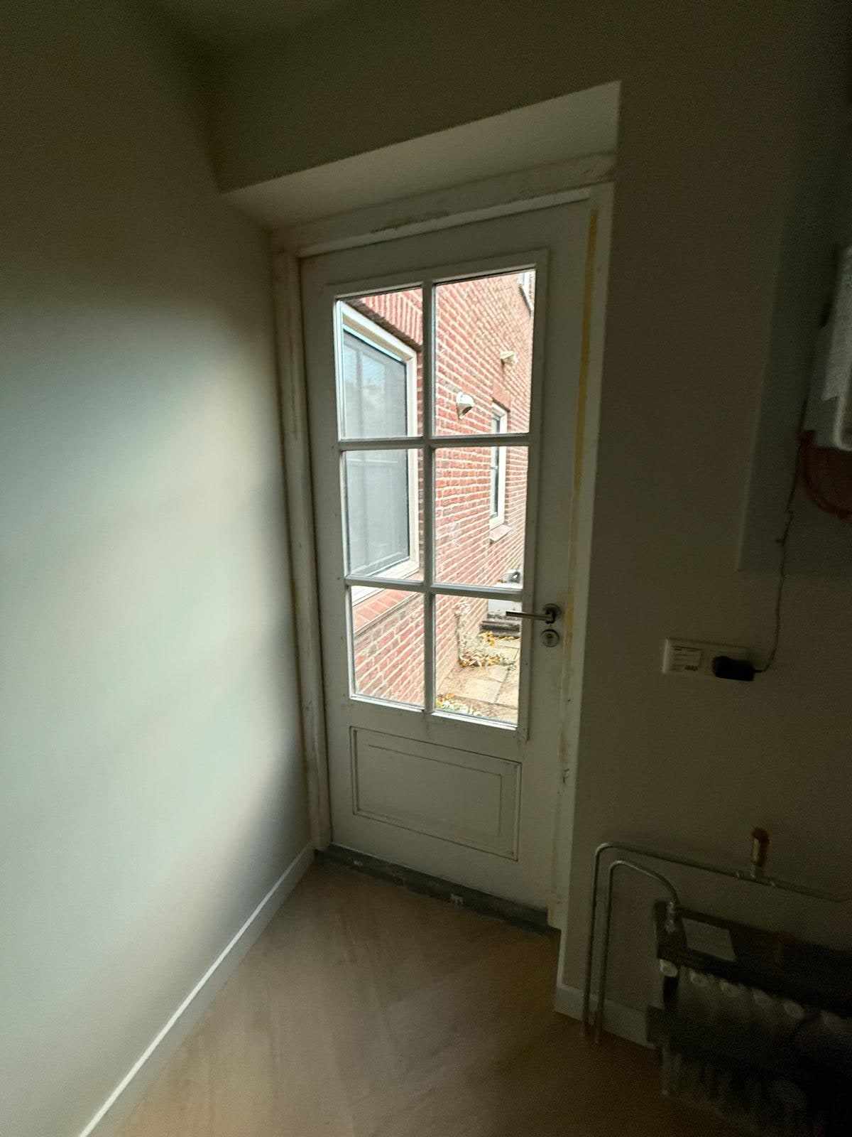 Wit gelakte achterdeur met glasroeden in een egaal geschilderde wand