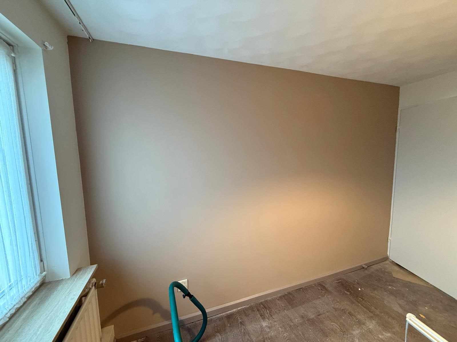 Taupe wand met raam en een slang op de vloer tijdens het schilderen