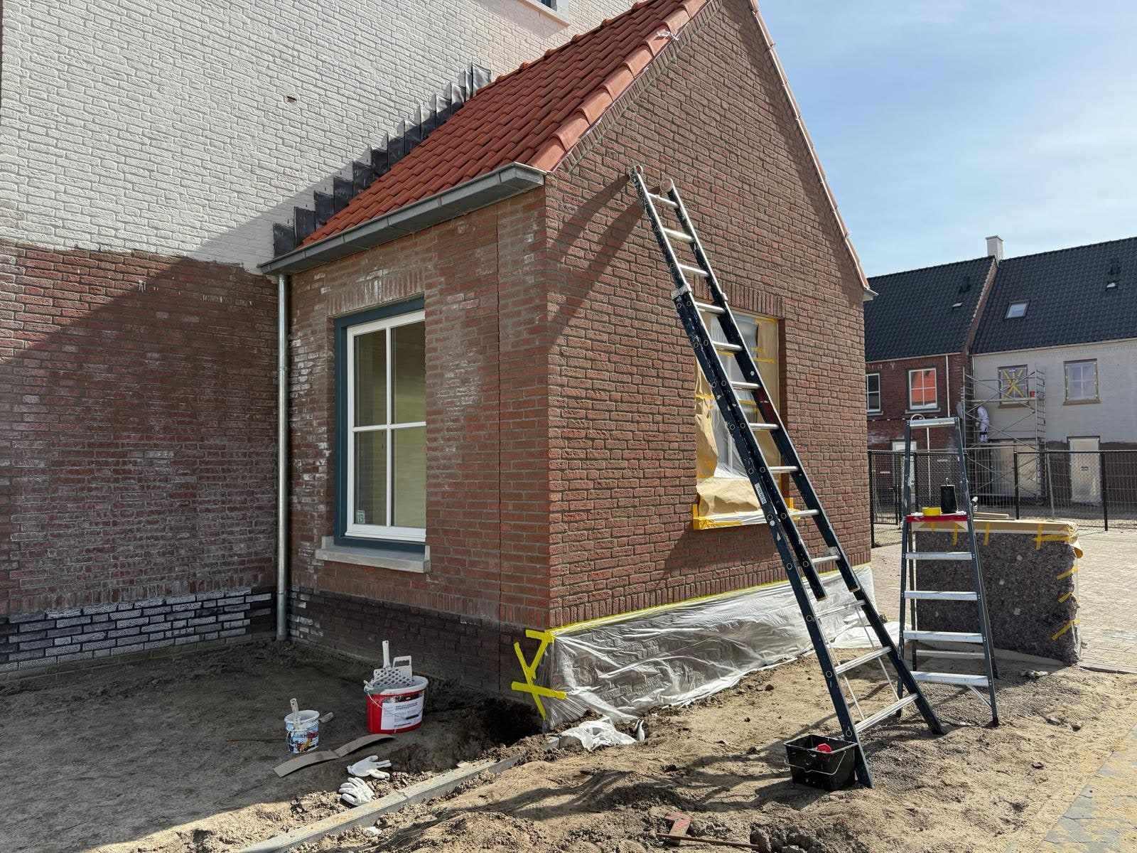 Rode gevel met afgeplakte kozijnen en ladders klaargezet voor het schilderwerk