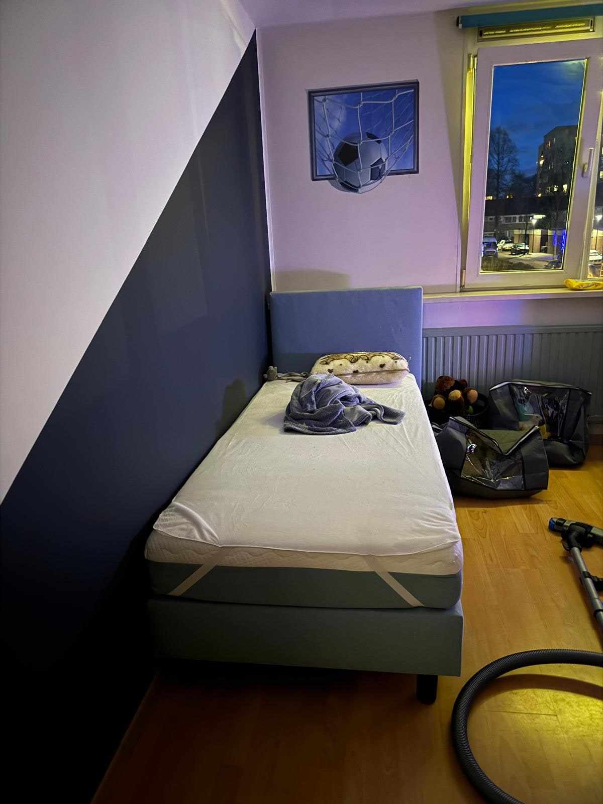 Slaapkamer met donkerblauwe diagonaal langs het bed en een raam aan de zijkant