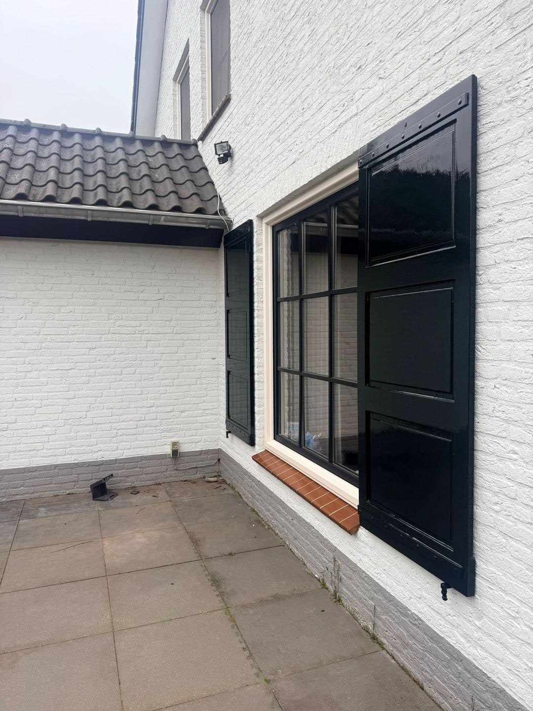Raam met opengeslagen donkere luiken in de witte gevel, terras ervoor
