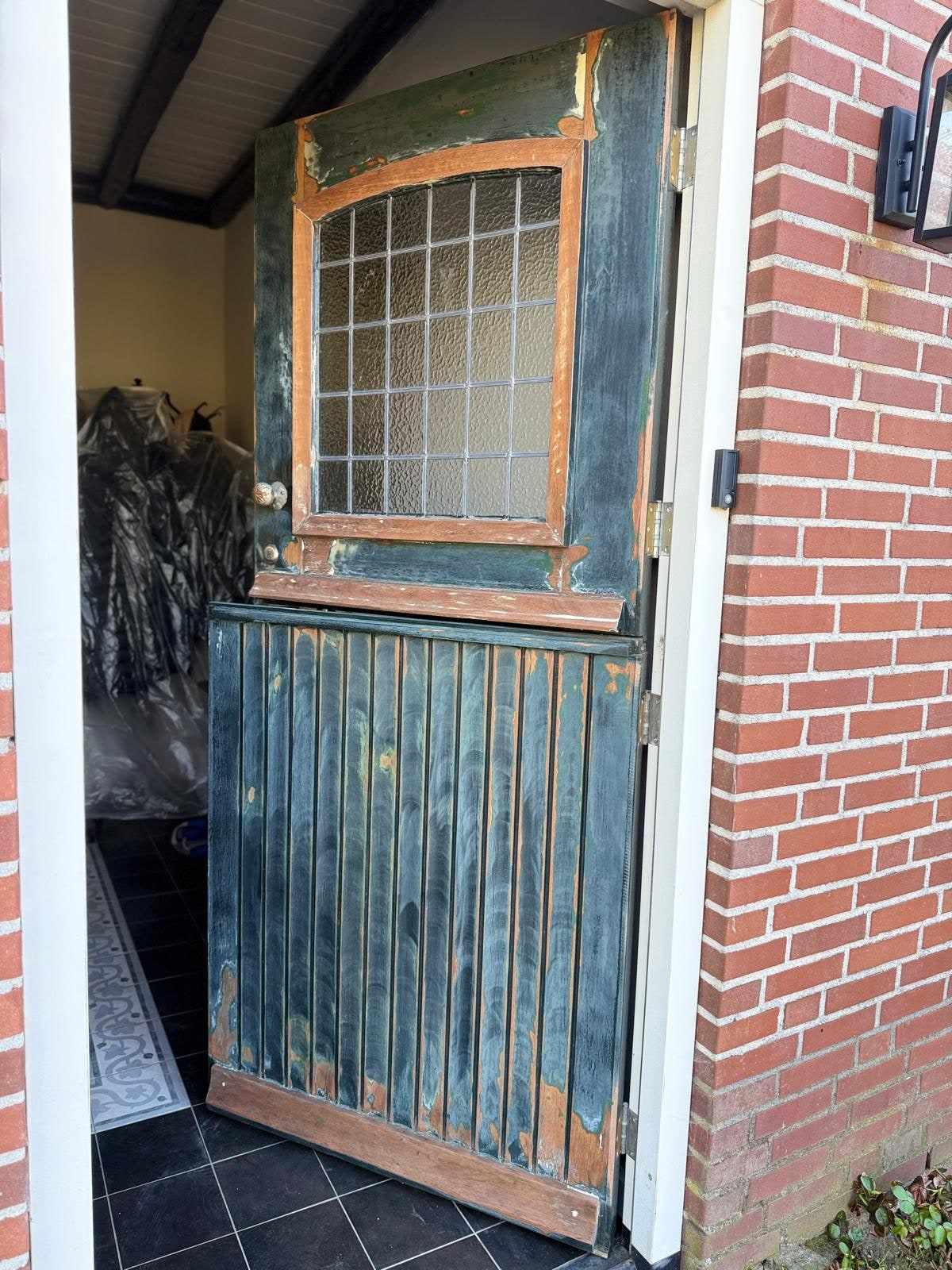 Oude buitendeur met afgebladderde verf en kaal hout rond het glas-in-loodraam