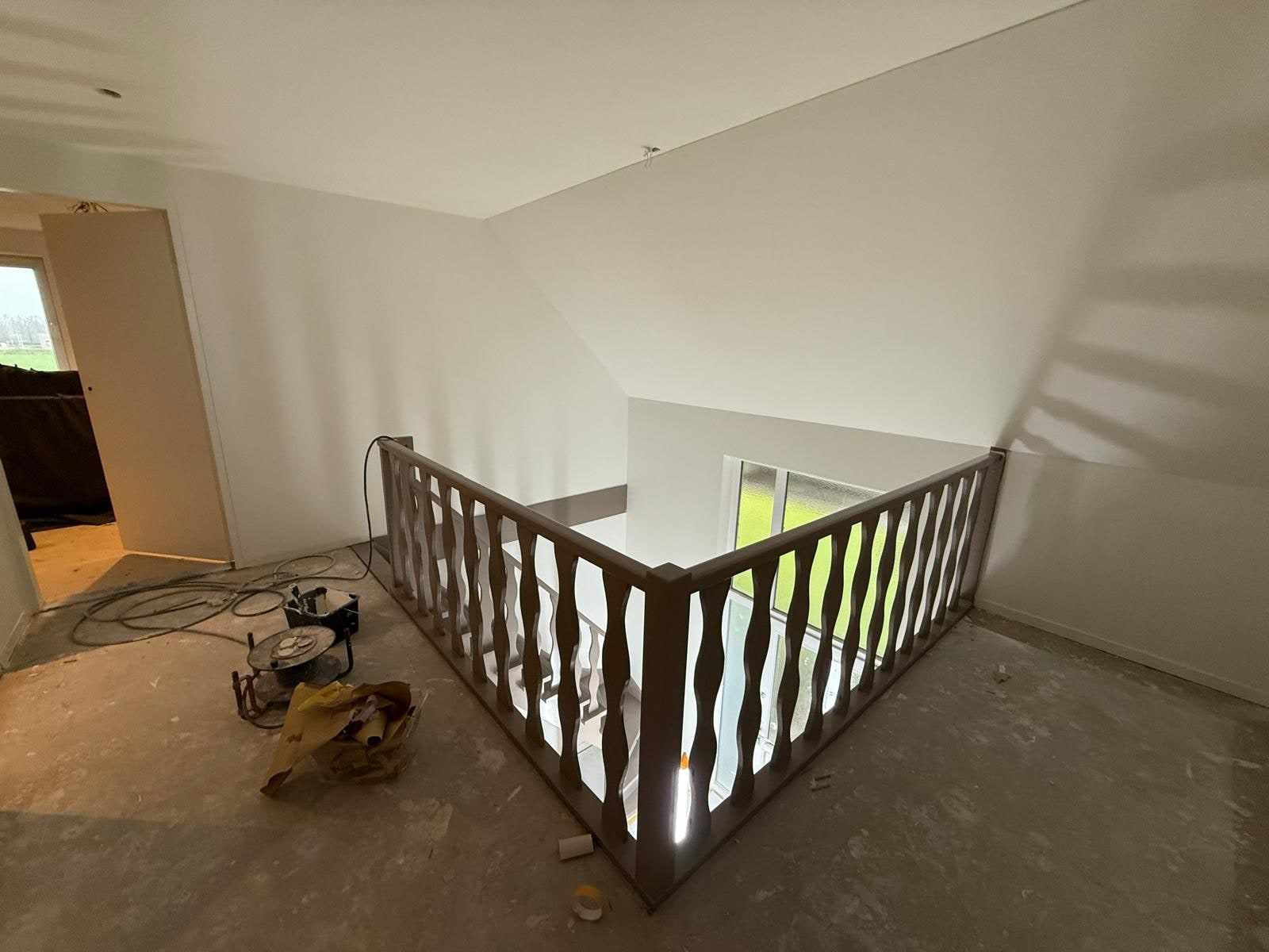 Overloop met houten balustrade tegen de pas witgeschilderde schuine wand