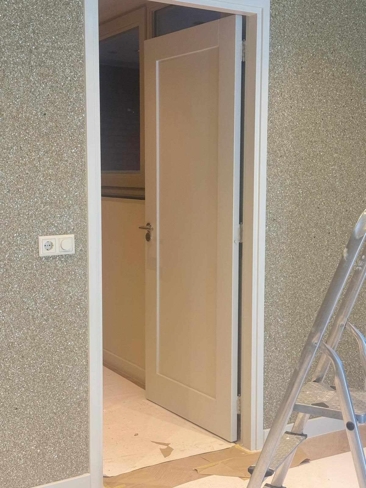 Deurkozijn tegen de grijze structuurwand, met een trapladder ernaast