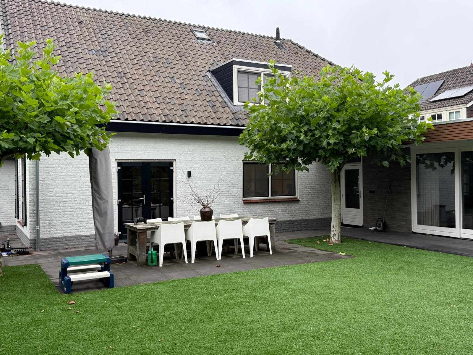 Witte achtergevel met terras, tuinmeubels en leibomen ervoor