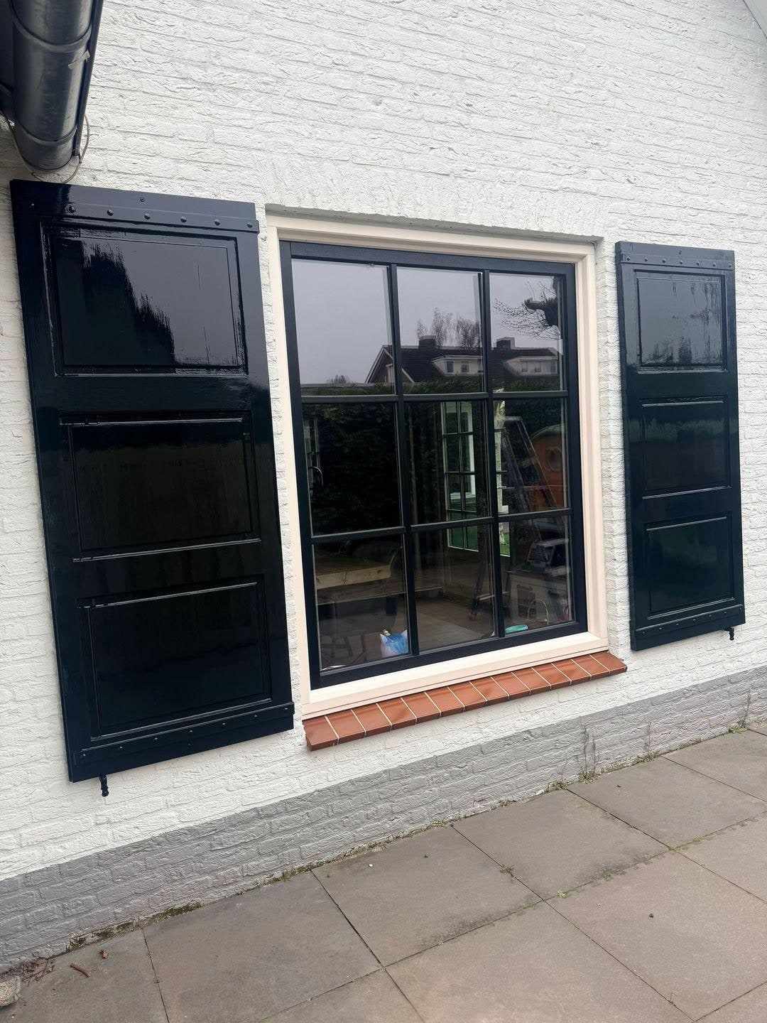 Raampartij van dichtbij met zwarte roeden, wit kozijn en donkere luiken